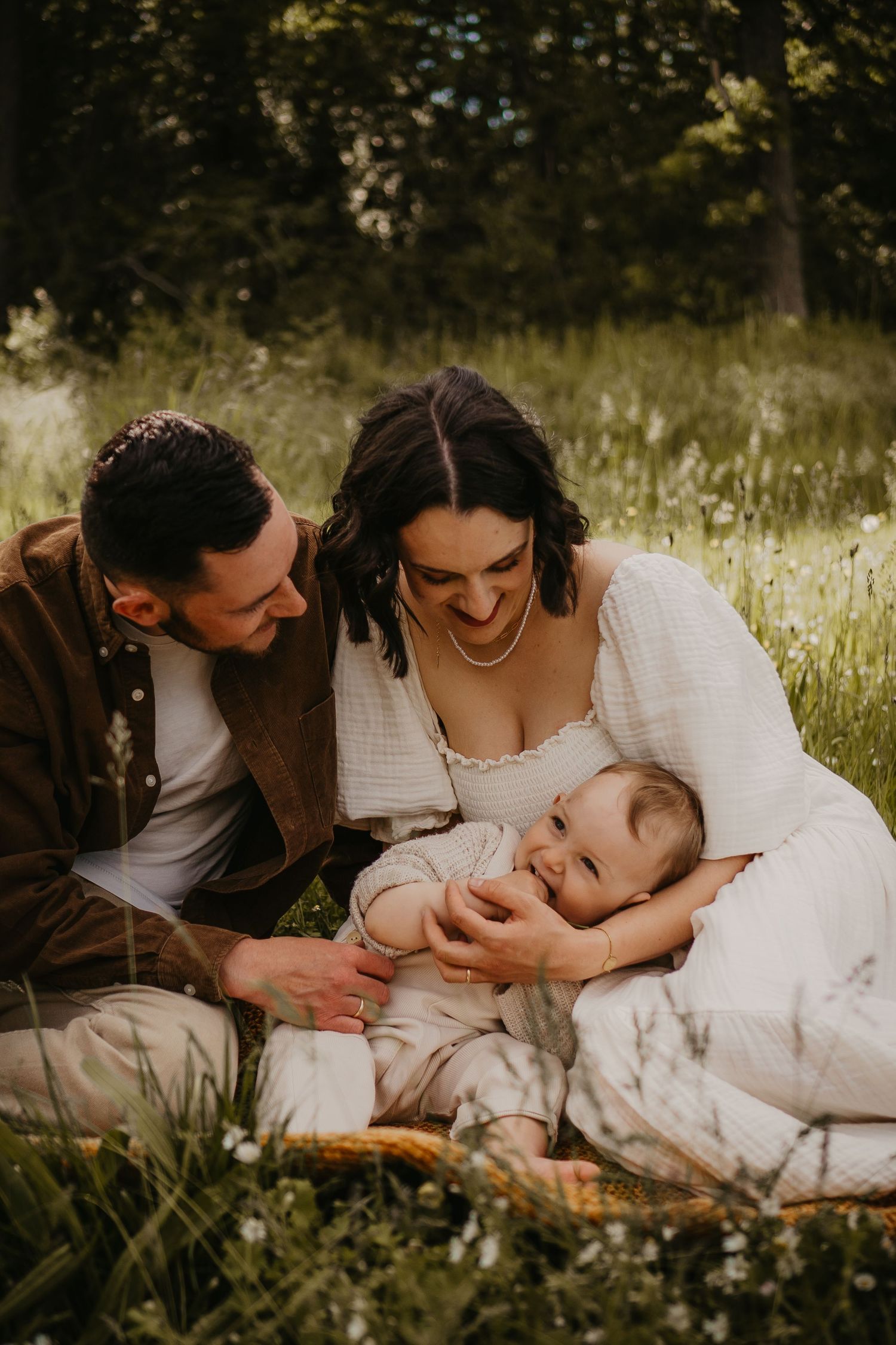 Family having tender outdoor picnic moment together on blanket in wildflower meadow during golden hour.