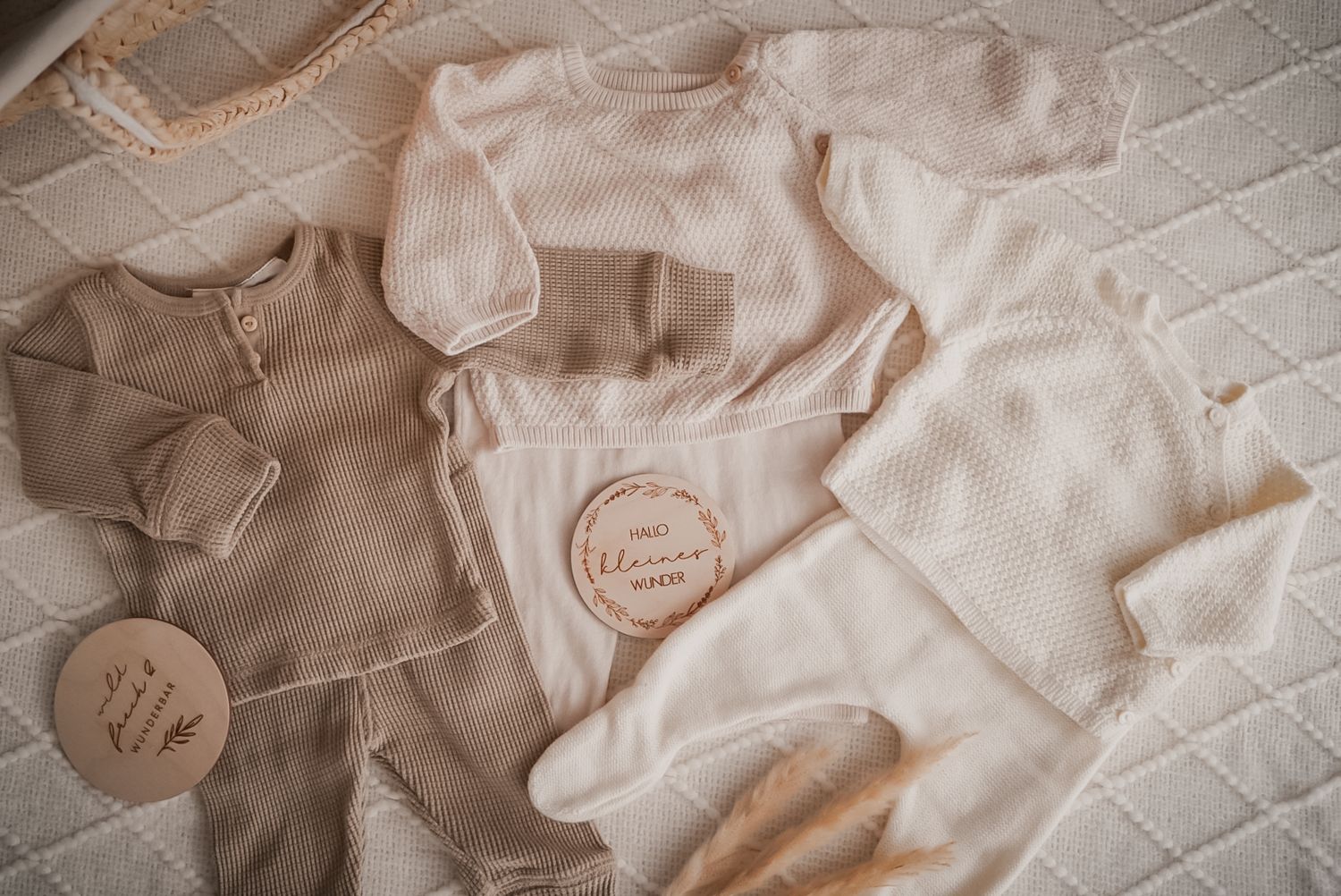 Soft neutral beige and cream colored baby clothes arranged on textured fabric with circular patches.