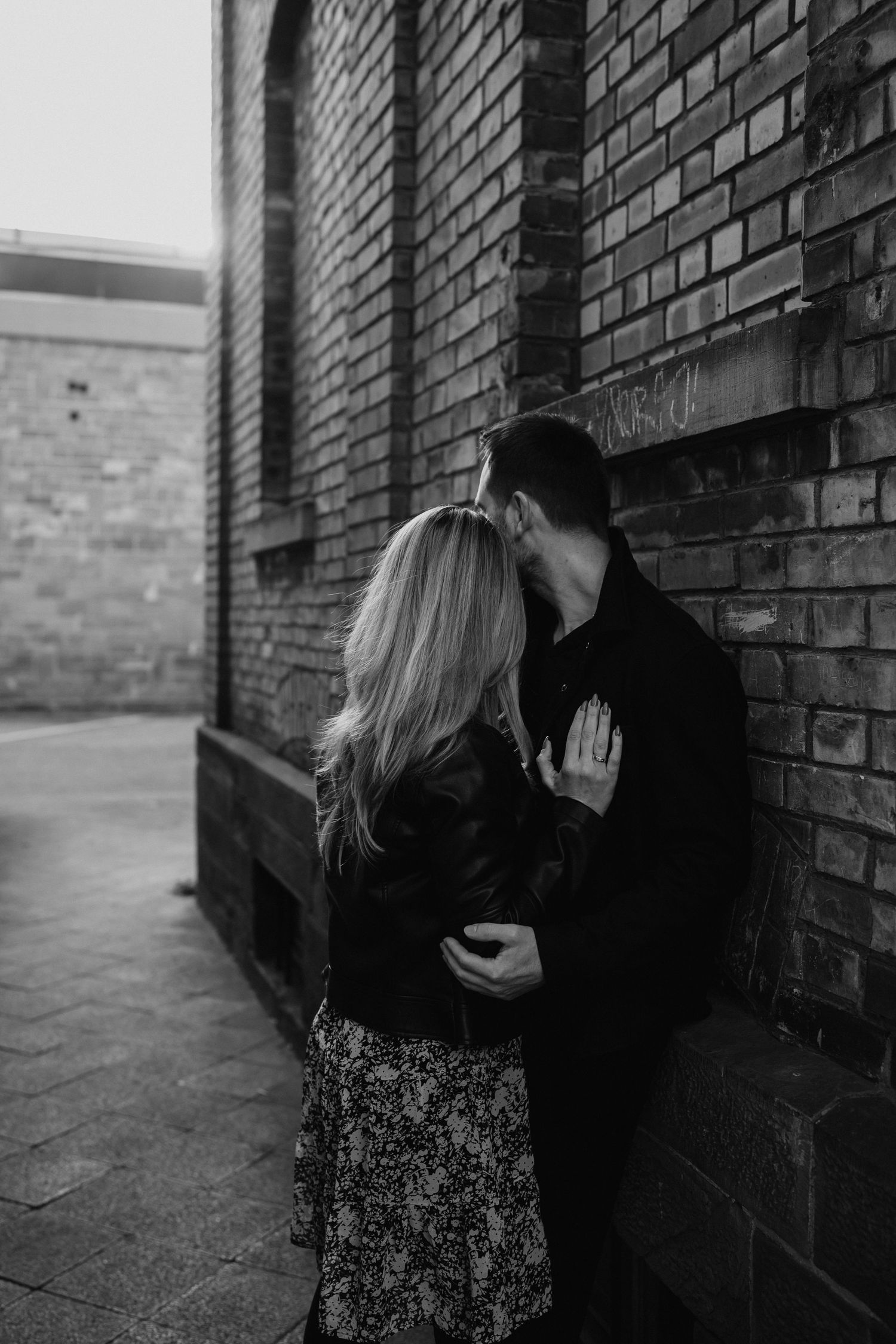 A couple embraces against a brick wall in a series of romantic black and white photographs.