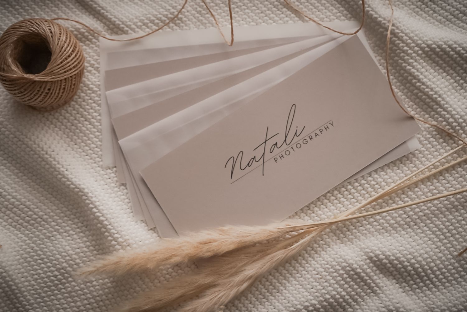 A white envelope with elegant script handwriting sits beside twine and dried wheat on a textured fabric background.