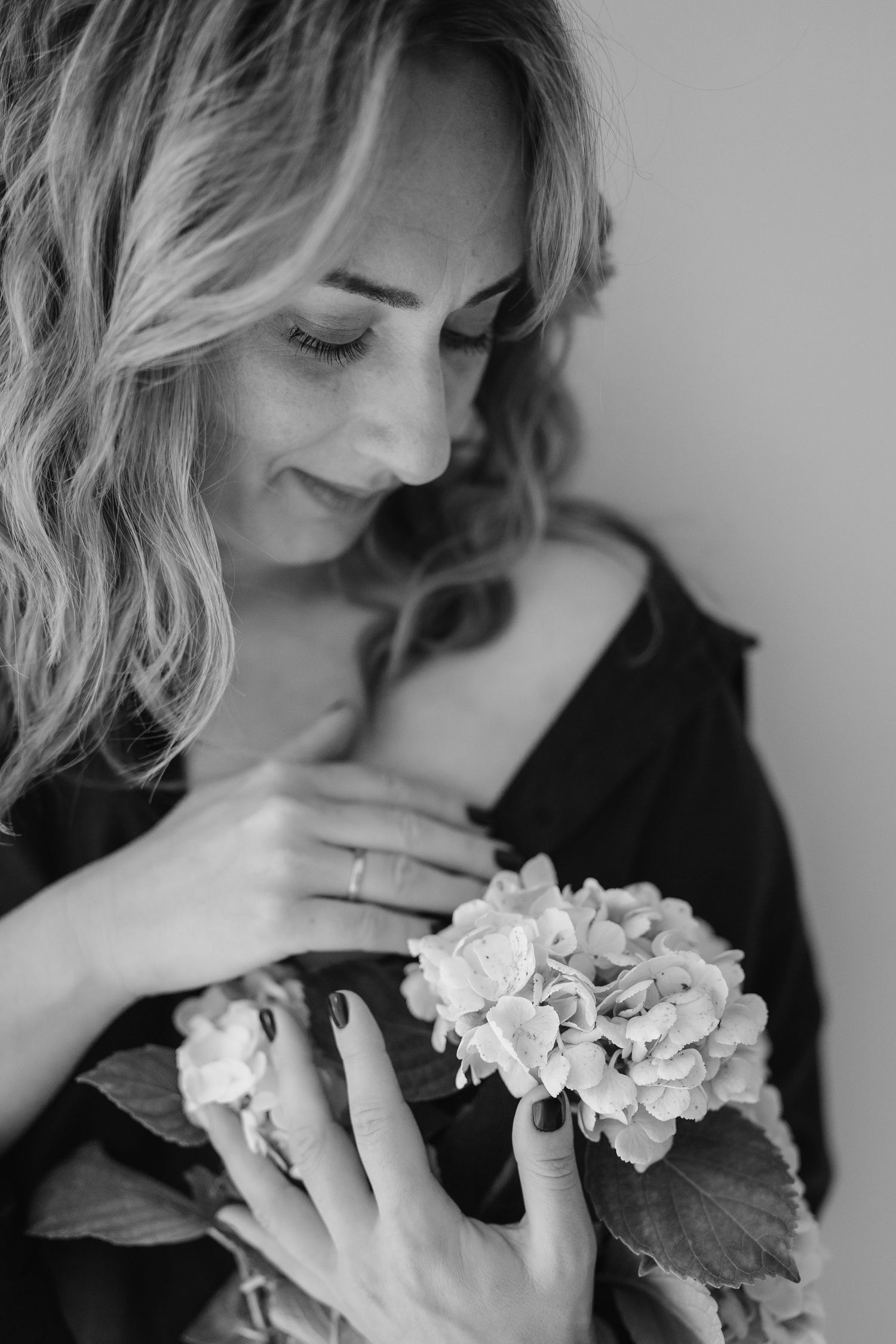 Black and white artistic portrait showing wavy blonde hair and gentle hands holding a delicate white hydrangea bloom.