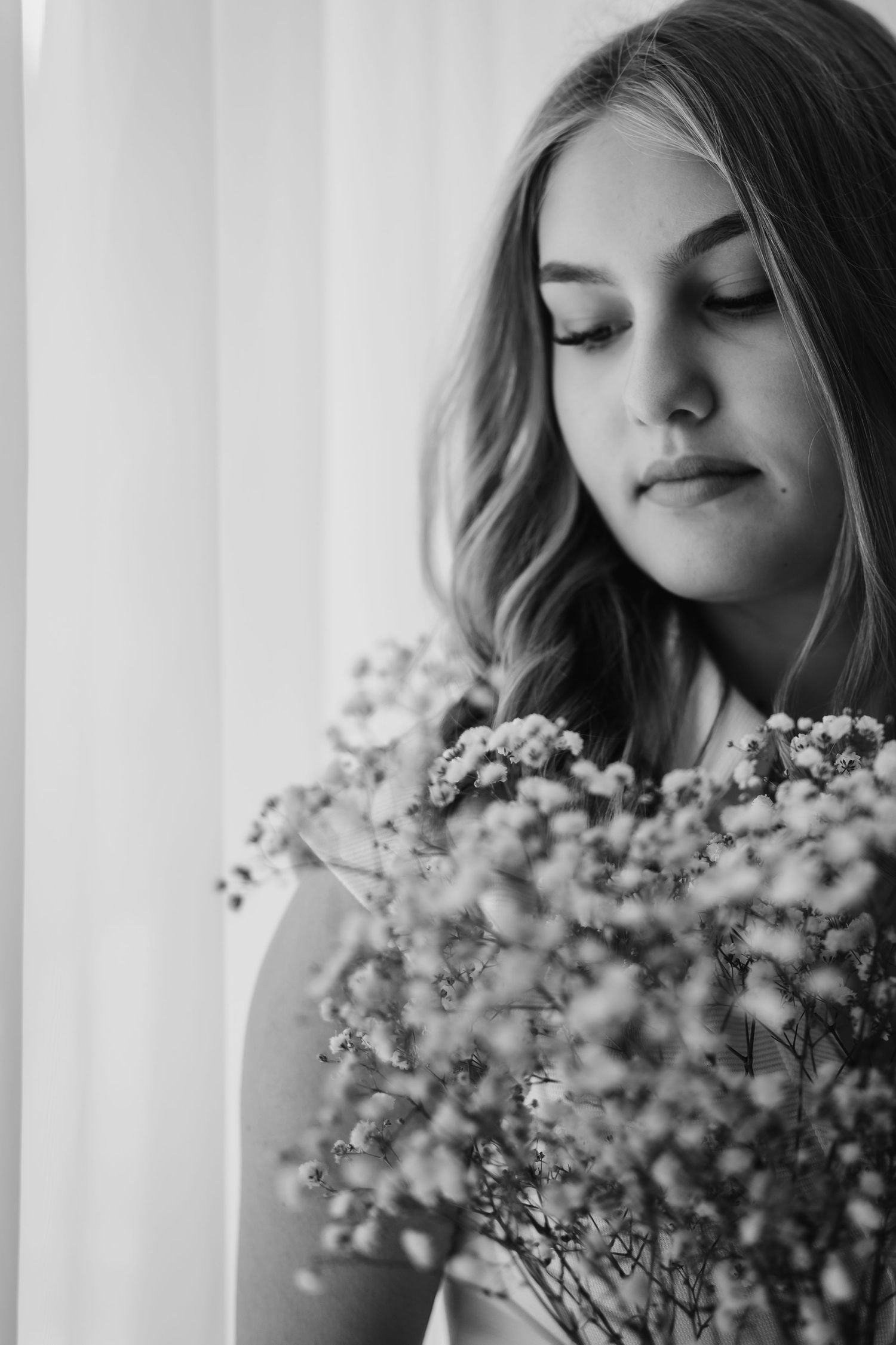 A black and white portrait series showing delicate baby's breath flowers held near a person's face in soft natural light.