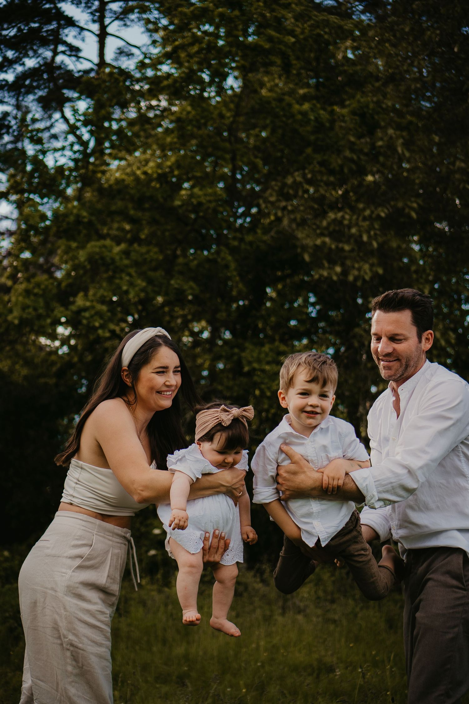 Candid family portrait in nature with parents lifting and playing with their two young children outdoors.