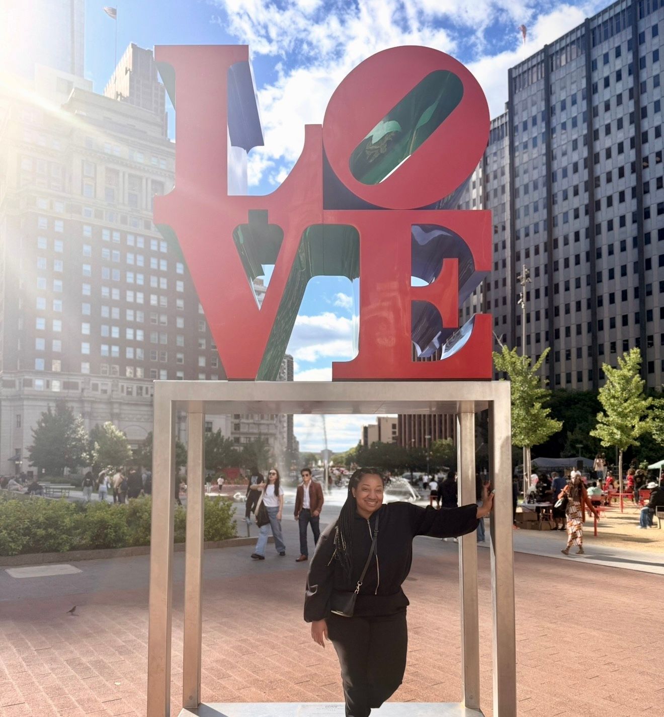 Person posing in front of the iconic red LOVE sculpture in an urban city plaza.