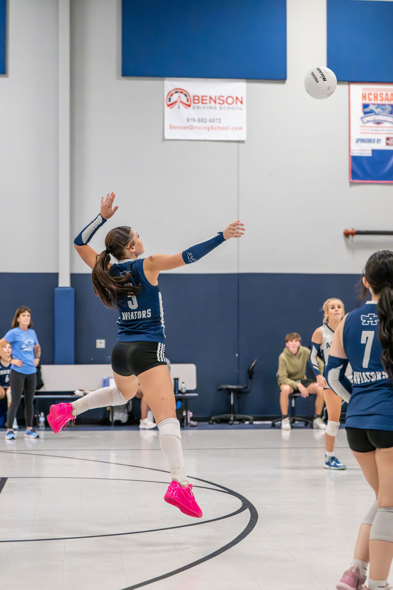 High school volleyball player jumping to serve during a match