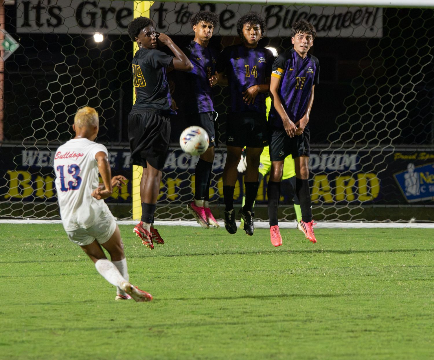 High school soccer player taking a free kick during a night game