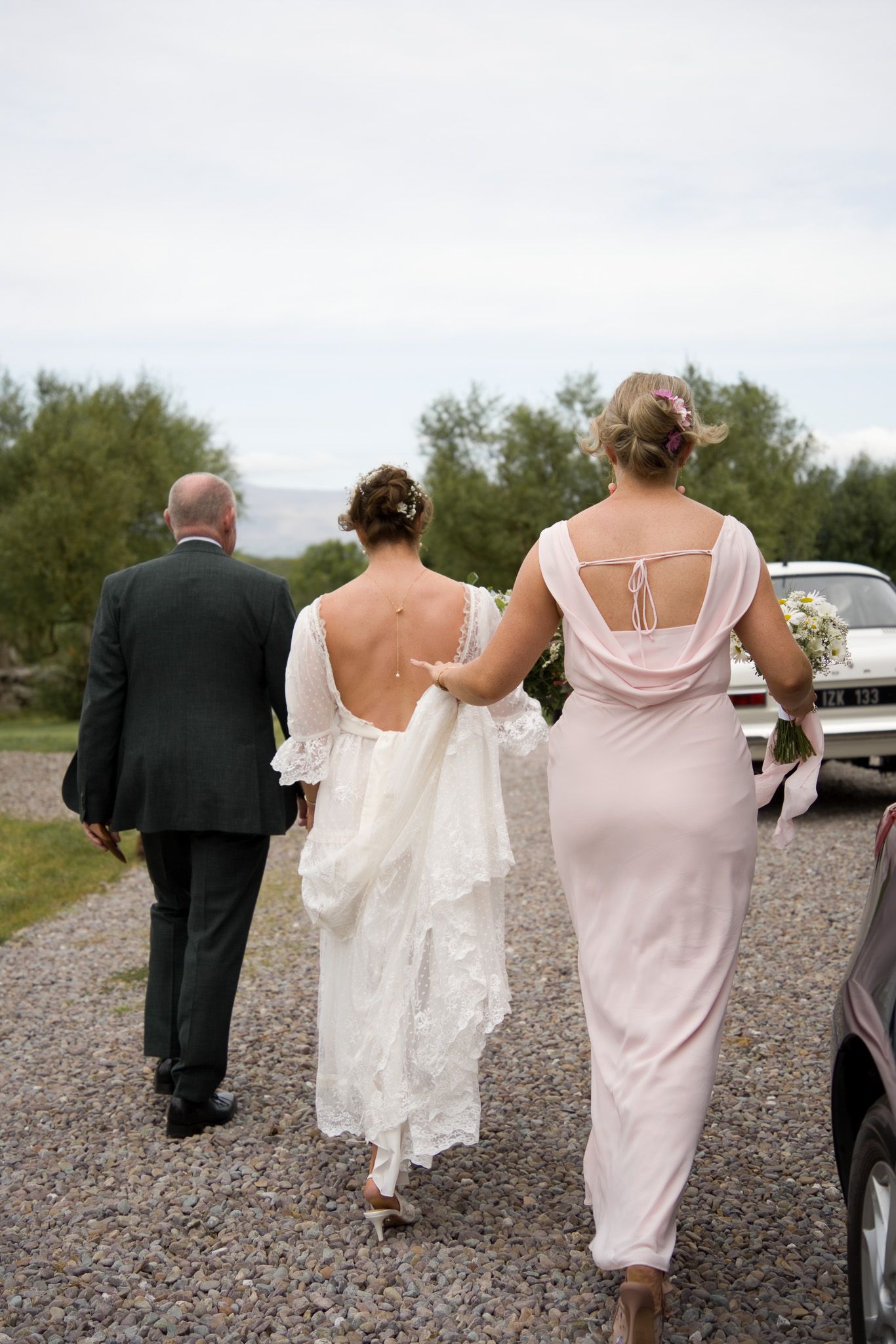 Bride walking arm in arm with her father and a bridesmaid in a blush dress