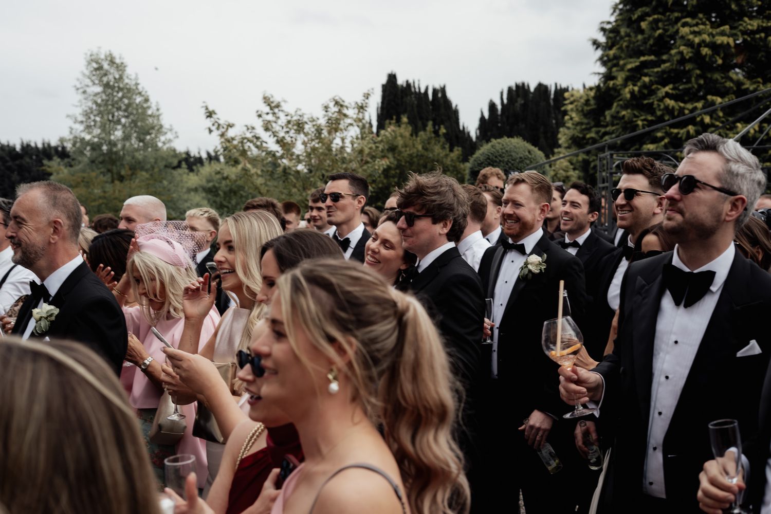 Wedding guests in black tie laughing together during an outdoor celebration