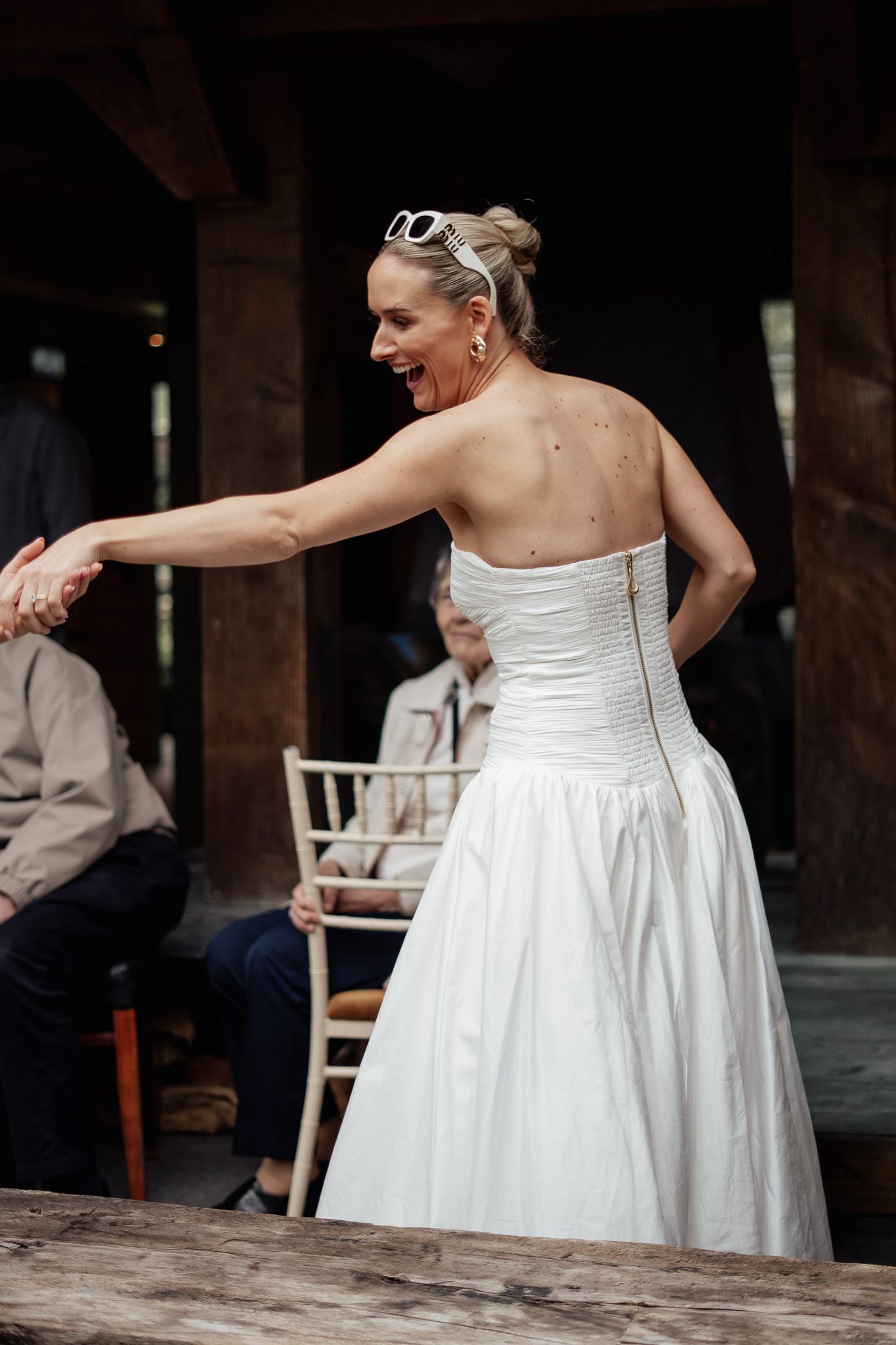 Bride laughing as she is pulled onto the dance floor by a guest