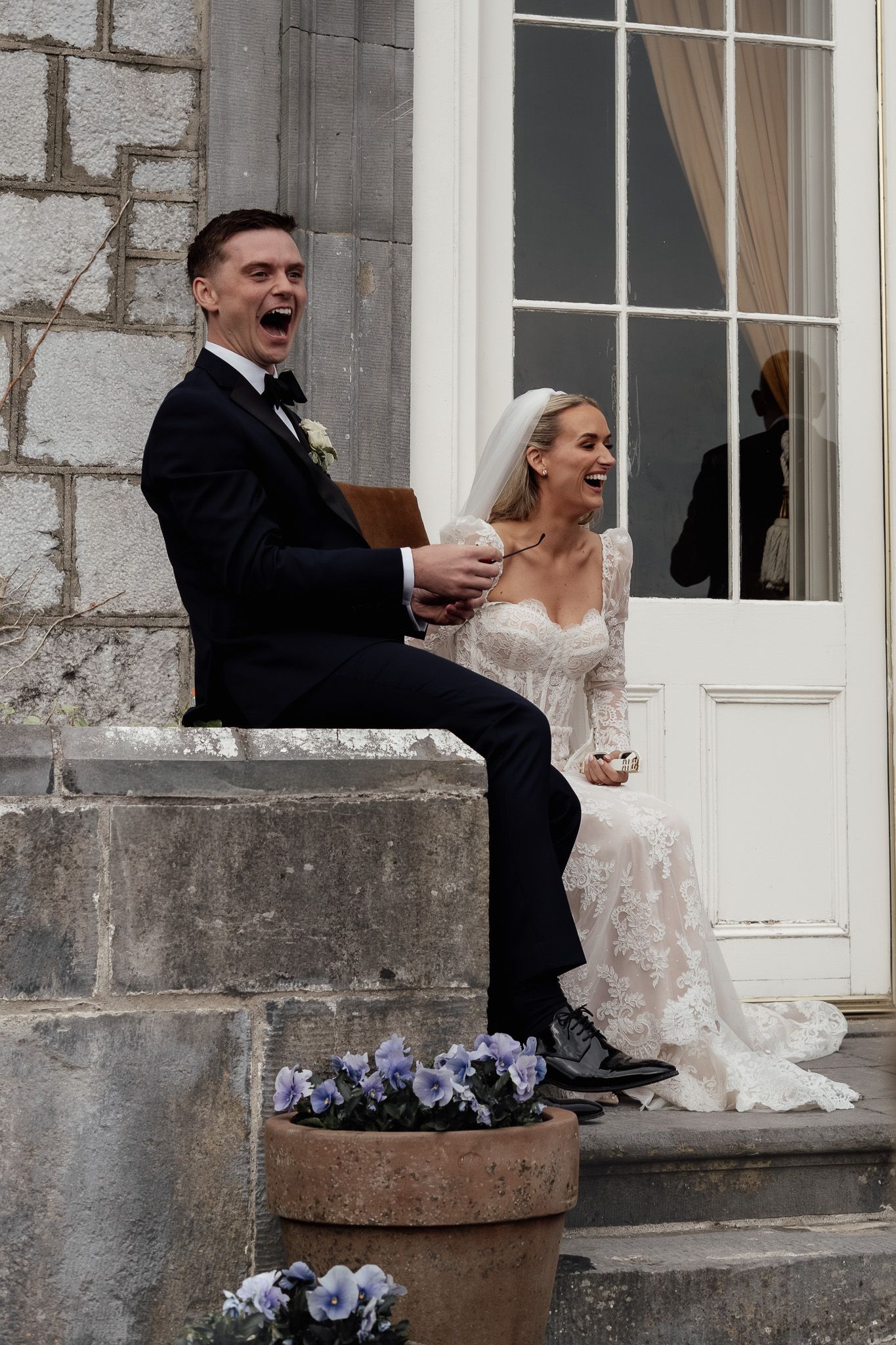 Bride and groom laughing together on stone steps outside their wedding venue