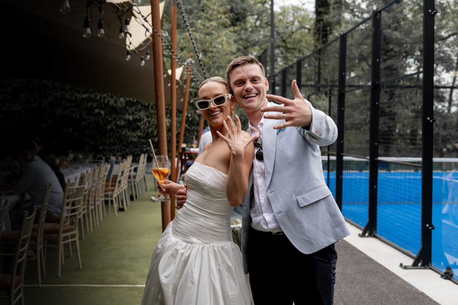 Bride and groom in sunglasses laughing and showing off their wedding rings