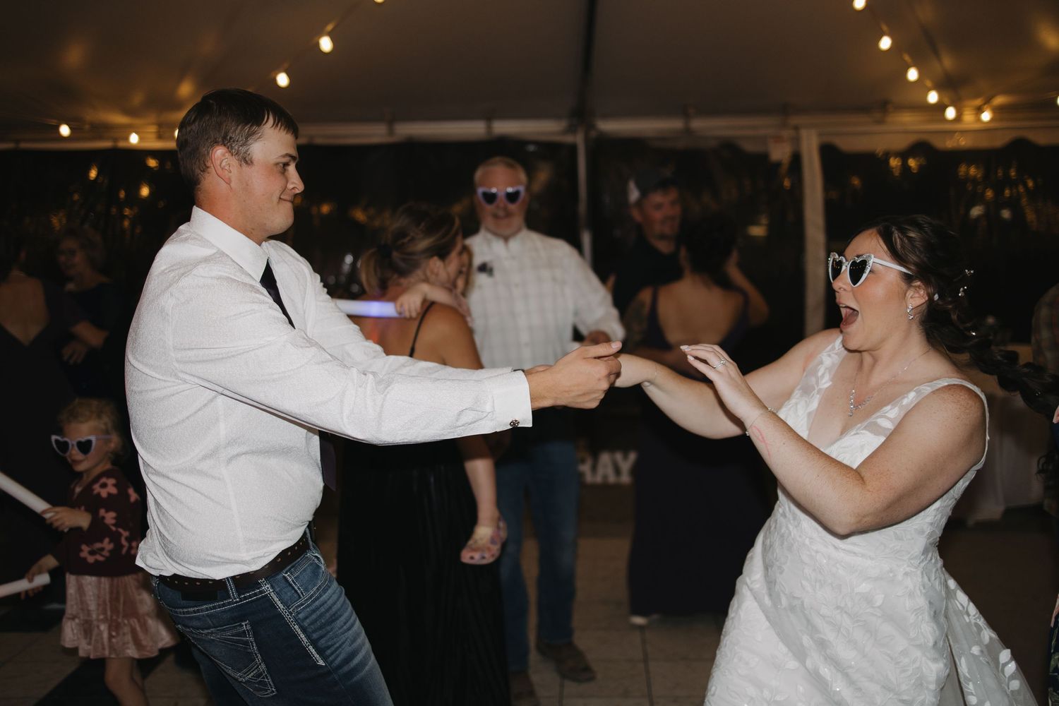 Bride and groom dance joyfully wearing sunglasses at lively outdoor wedding reception. Wyoming wedding.
