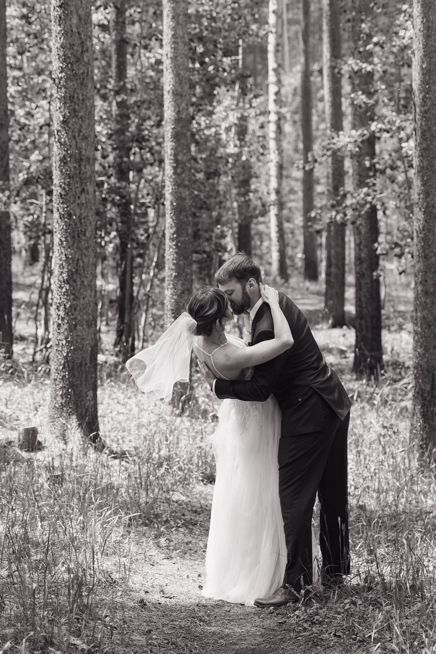 Black and white photo of a bride and groom sharing a kiss in a forest wedding.
