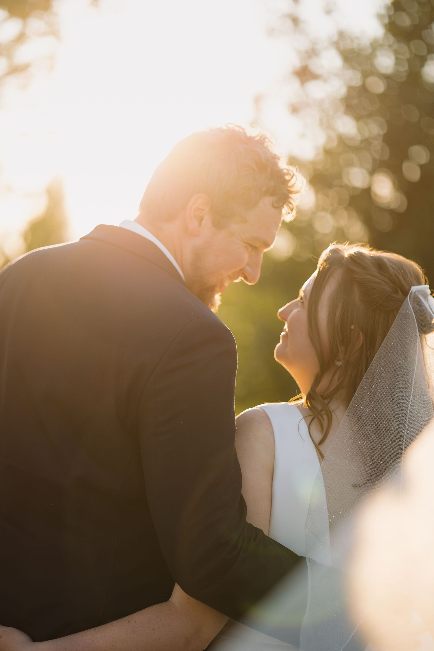 Bride and groom share an intimate moment bathed in warm golden sunlight during outdoor wedding portraits.