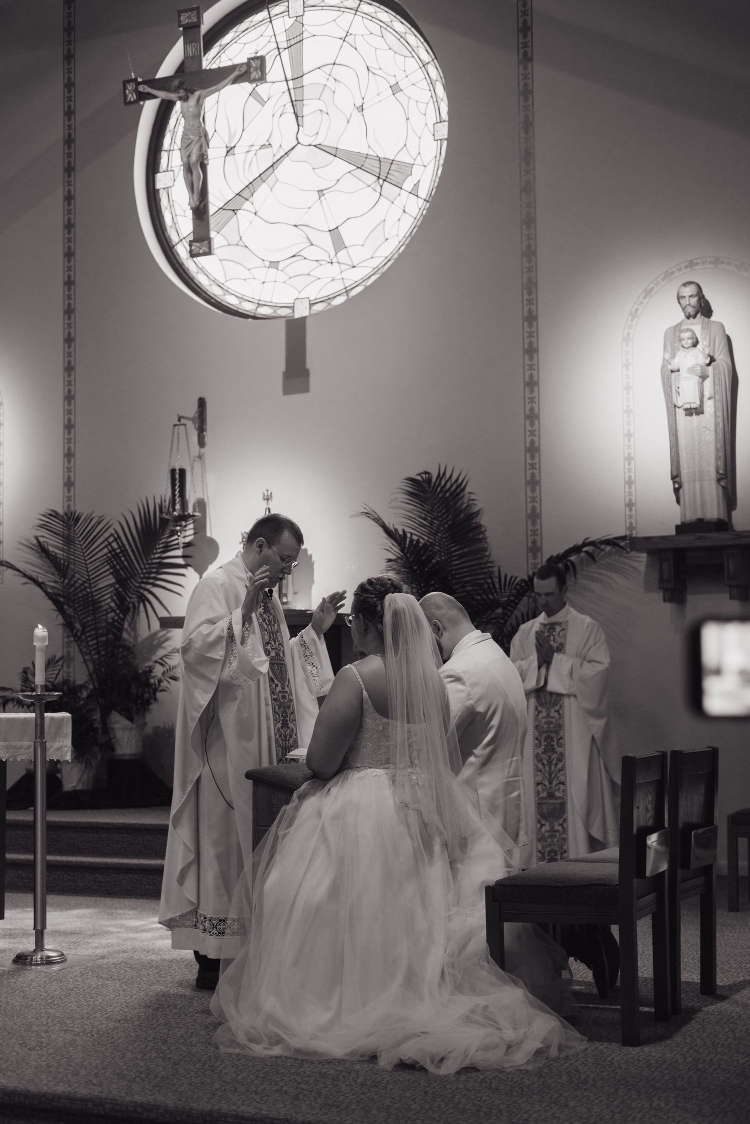 Black and white photo of a bride kneeling at the altar during a Catholic wedding ceremony.