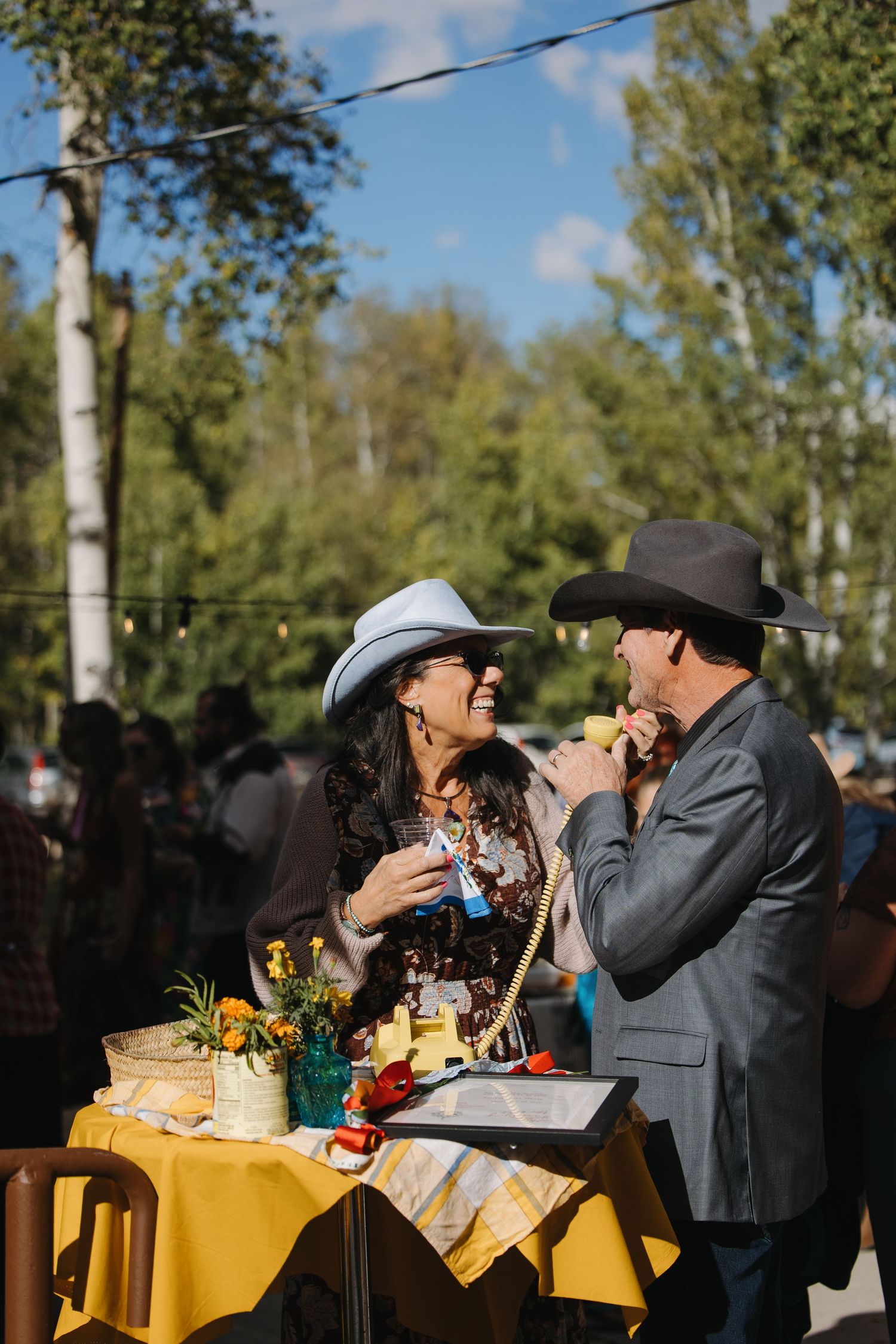 Couple in cowboy hats share a romantic moment at yellow-draped outdoor wedding reception table. Wyoming wedding.