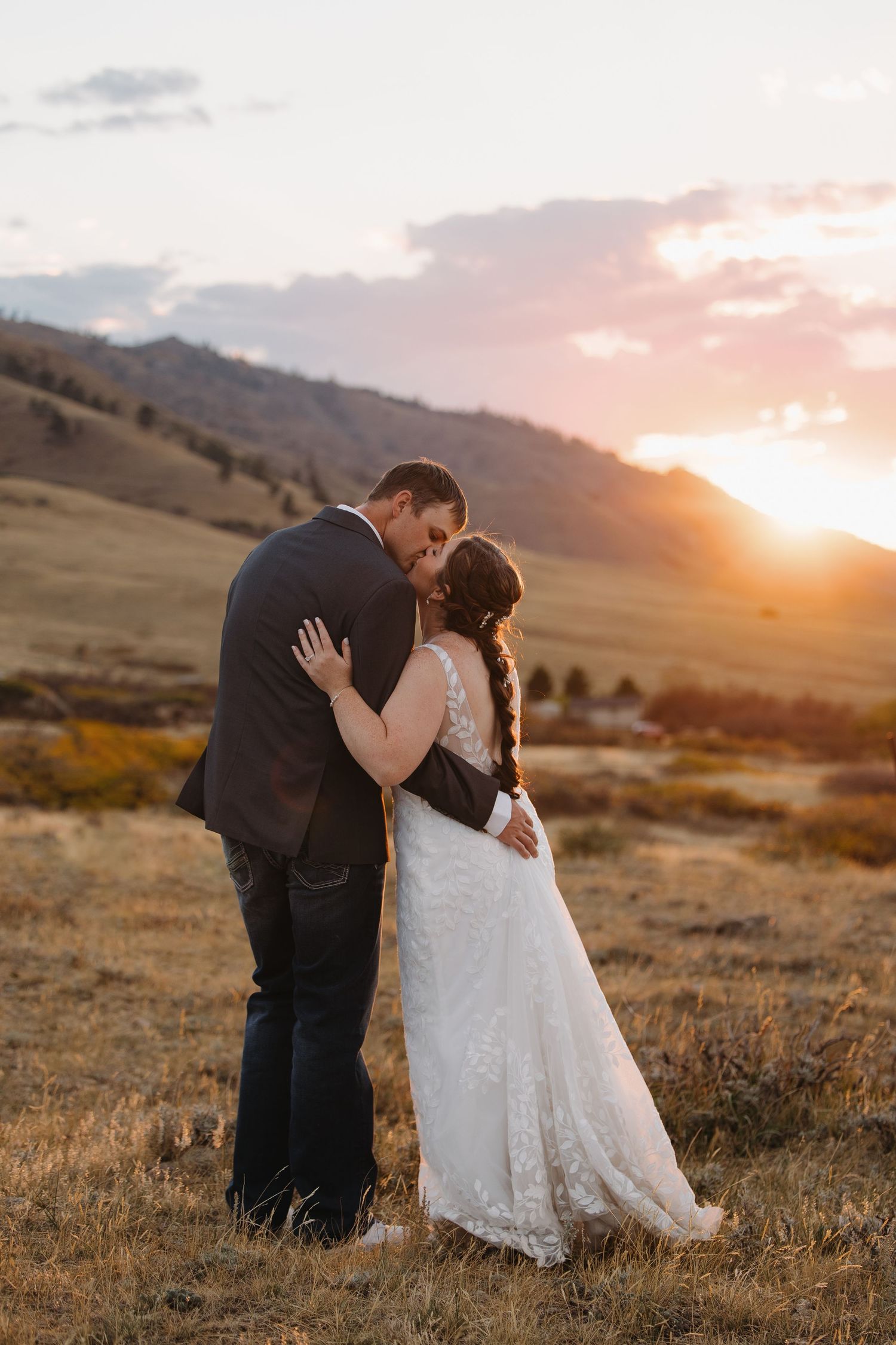 Bride and groom share a romantic kiss at golden sunset with mountain landscape backdrop. Wyoming wedding.
