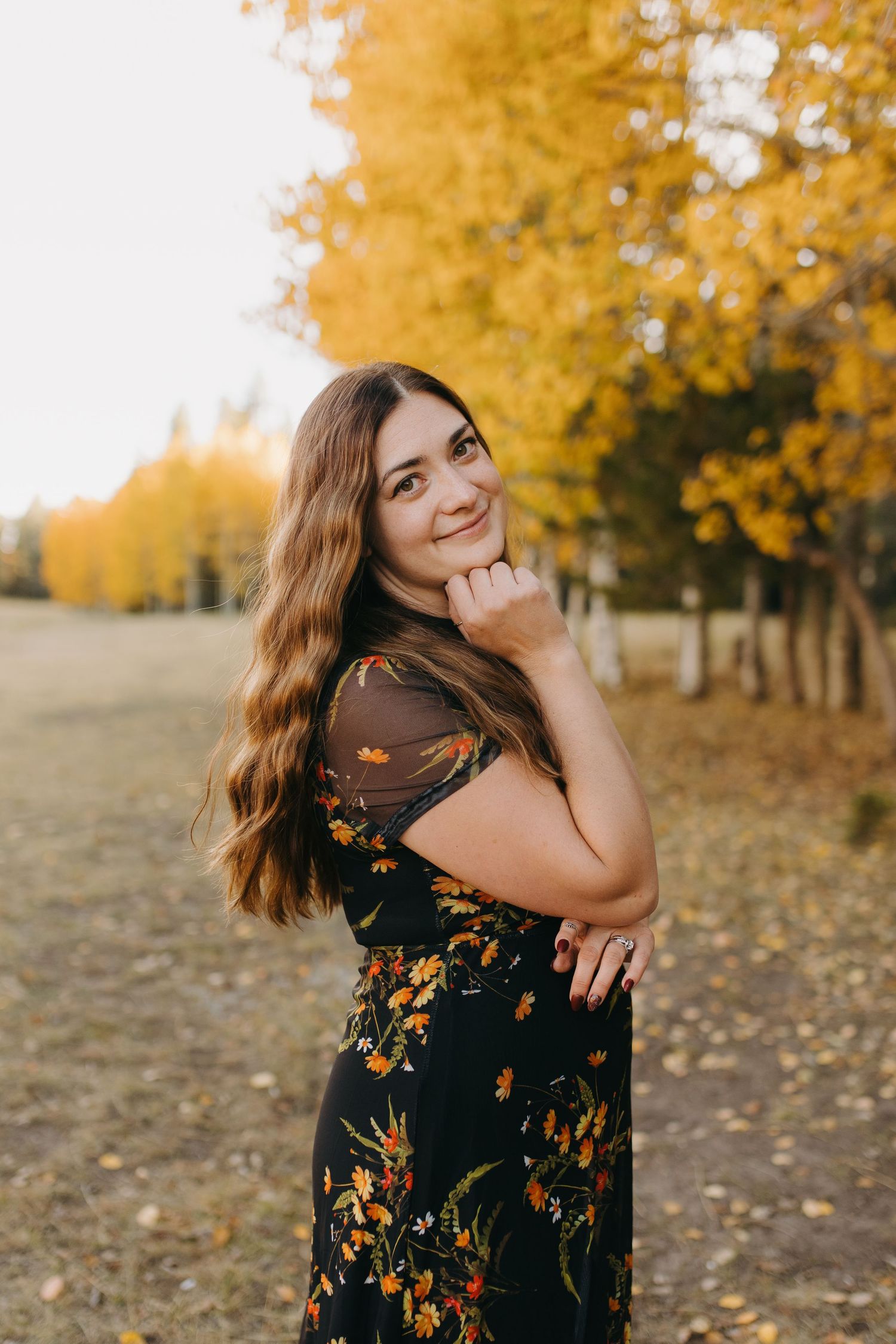 Young woman in black floral dress smiling outdoors among golden autumn aspen trees. Wyoming photographer.