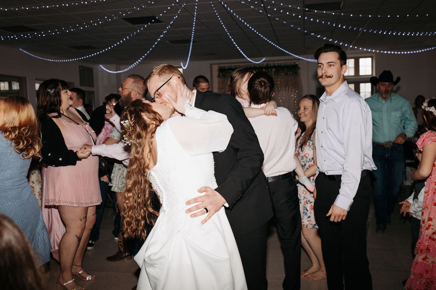 Bride and groom share a dance embrace surrounded by guests at their wedding reception.