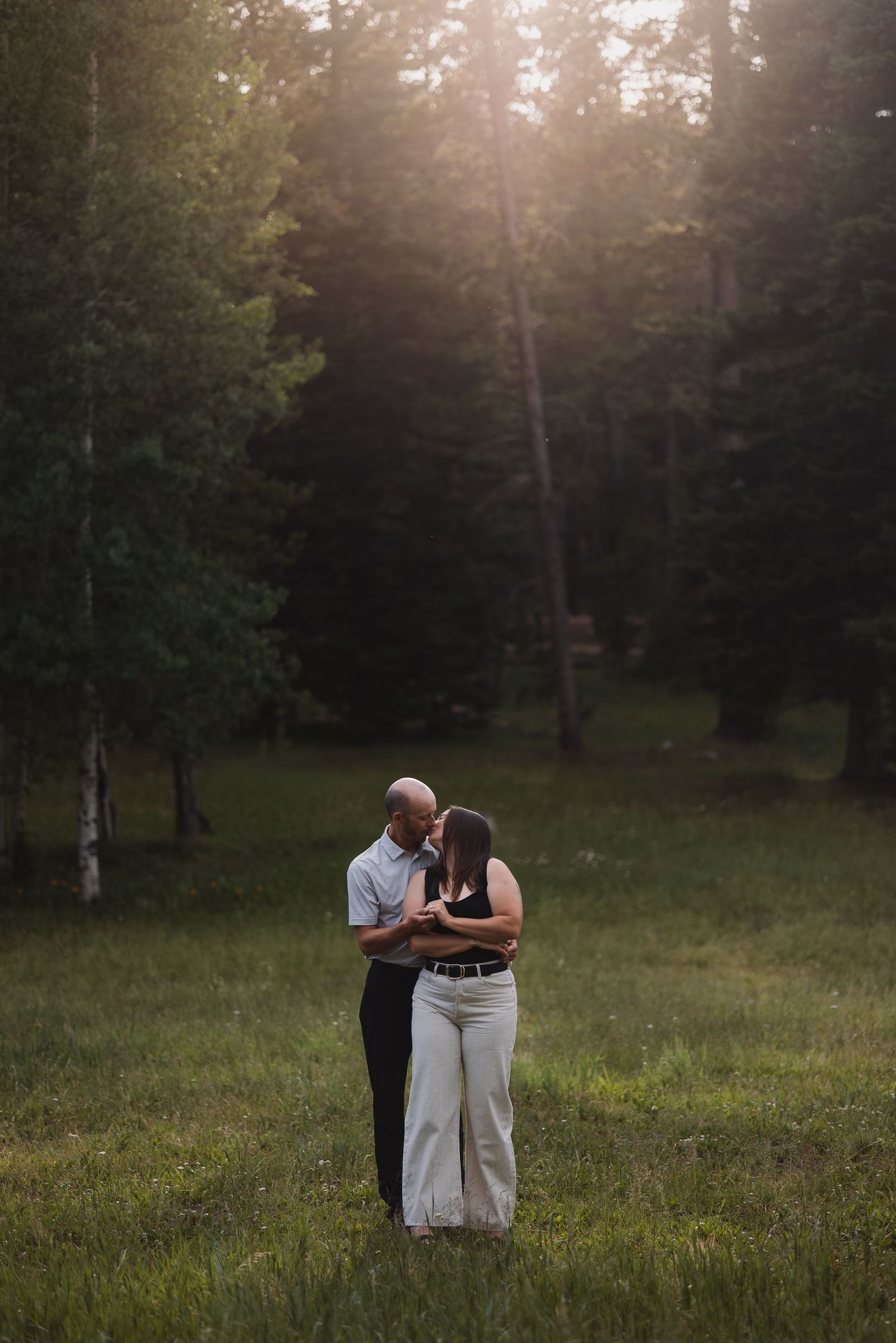Couple embracing romantically in a sunlit forest clearing at golden hour.