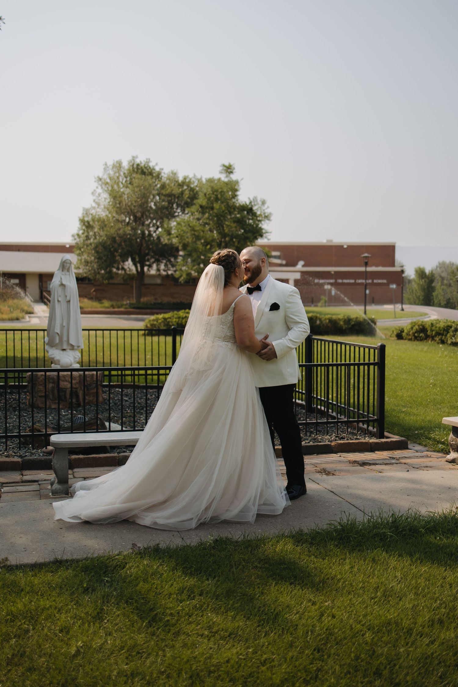Bride and groom sharing a romantic kiss outdoors near a garden statue after their wedding.