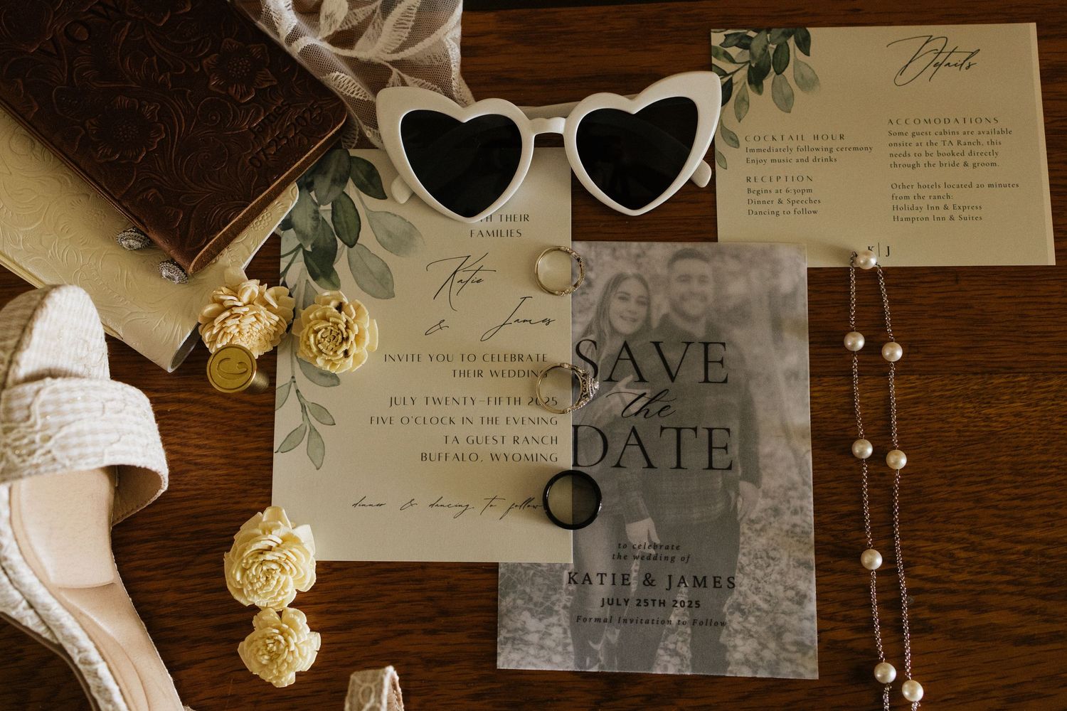 Flat lay of wedding details including save the date card, pearl necklace, rings, and heart sunglasses.