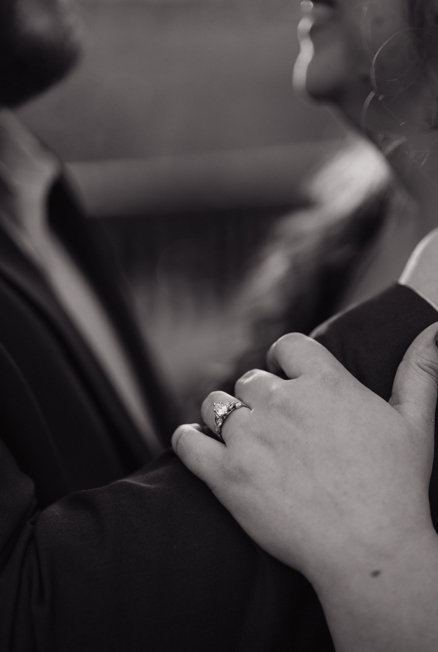 Black and white close-up of a woman's hand with engagement ring resting on a man's chest.