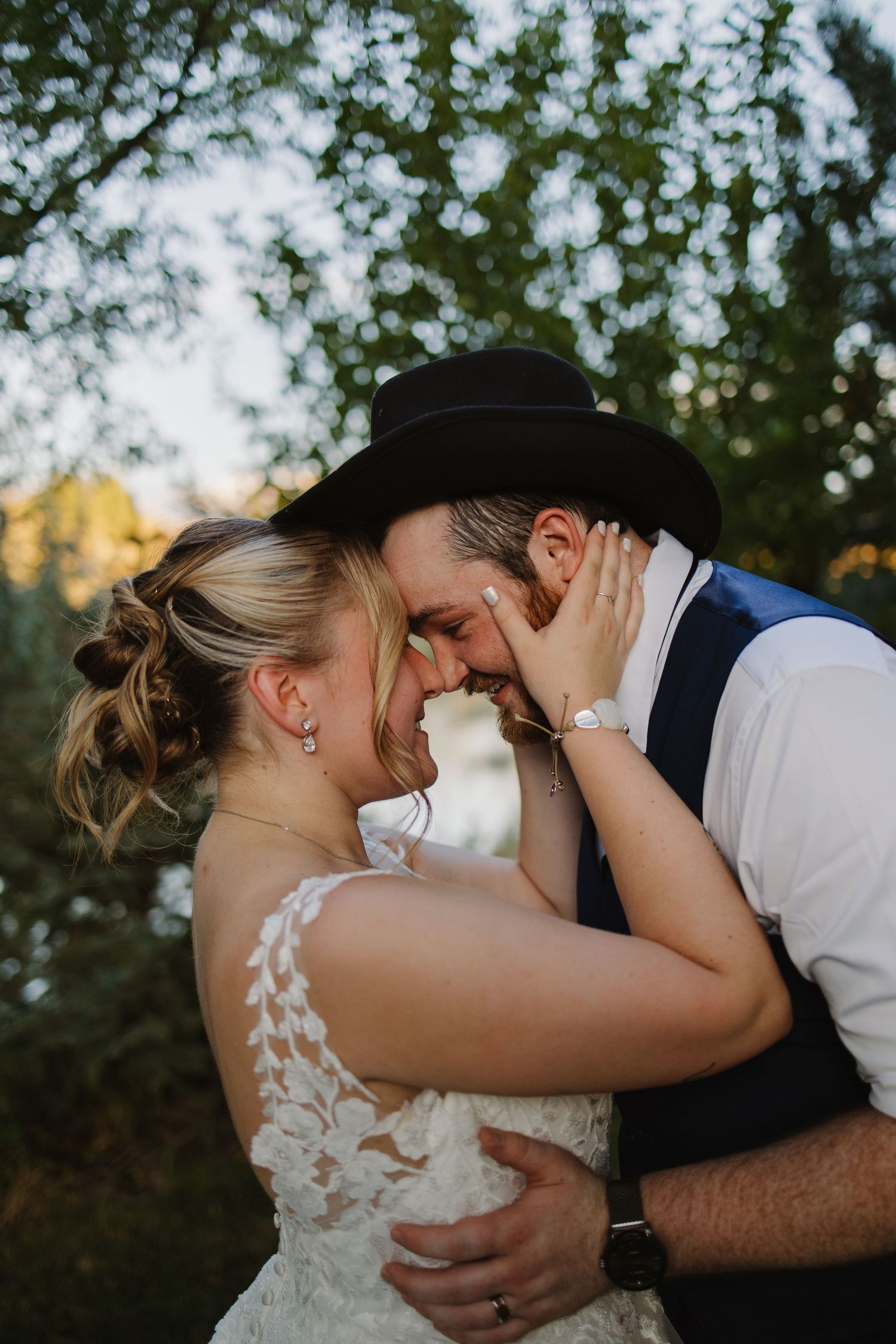 Bride and groom in black cowboy hat share an intimate forehead touch embrace outdoors at sunset.