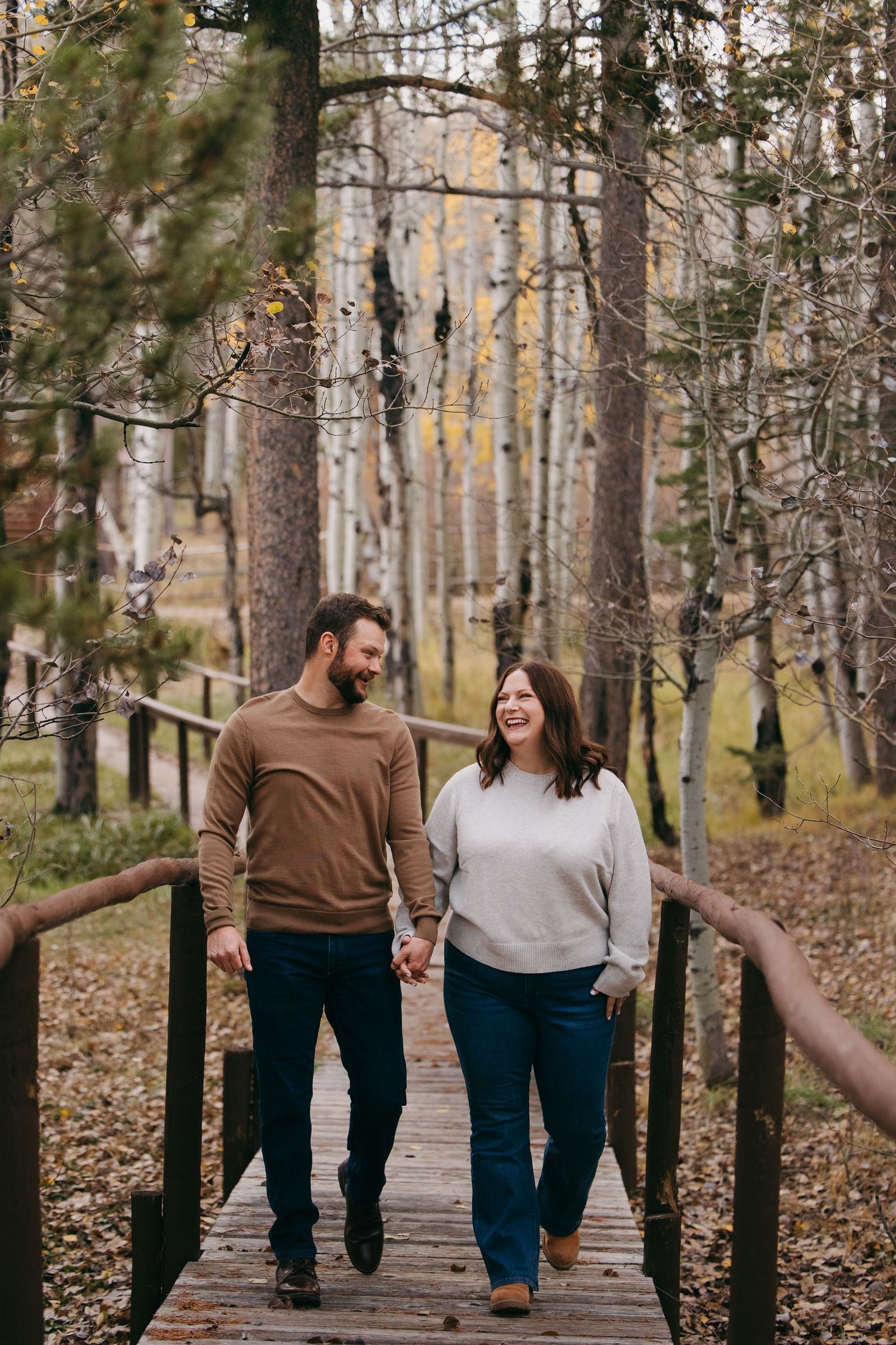 Happy couple holds hands walking across wooden bridge in colorful autumn forest. Wyoming