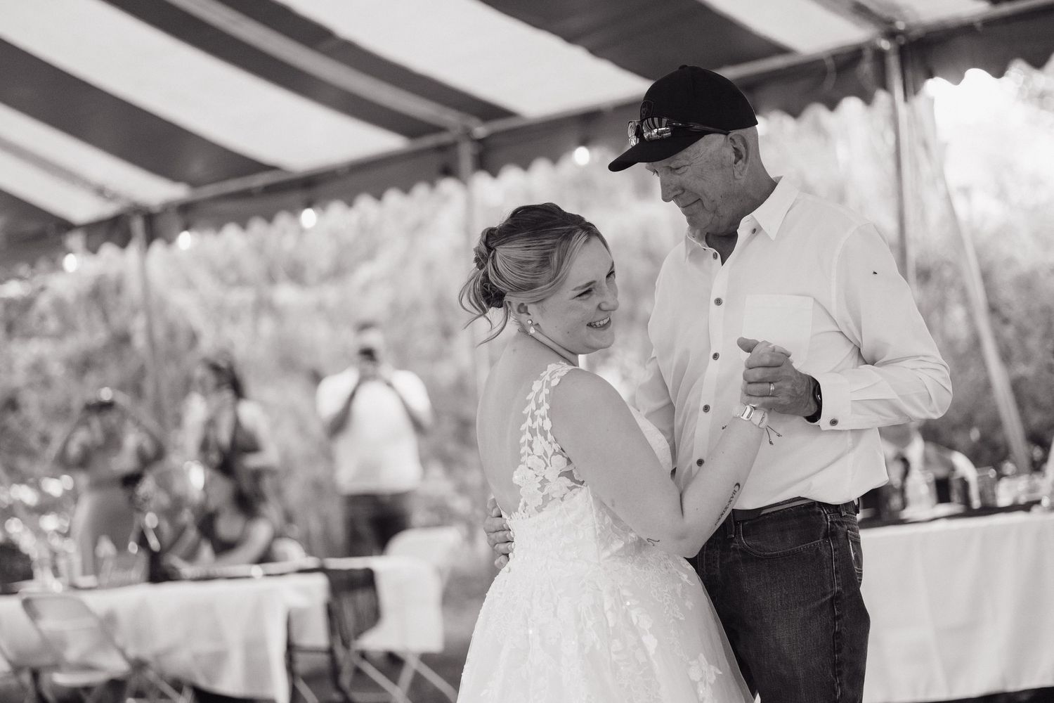 Black and white photo of a bride sharing a tender dance with her father at an outdoor reception.