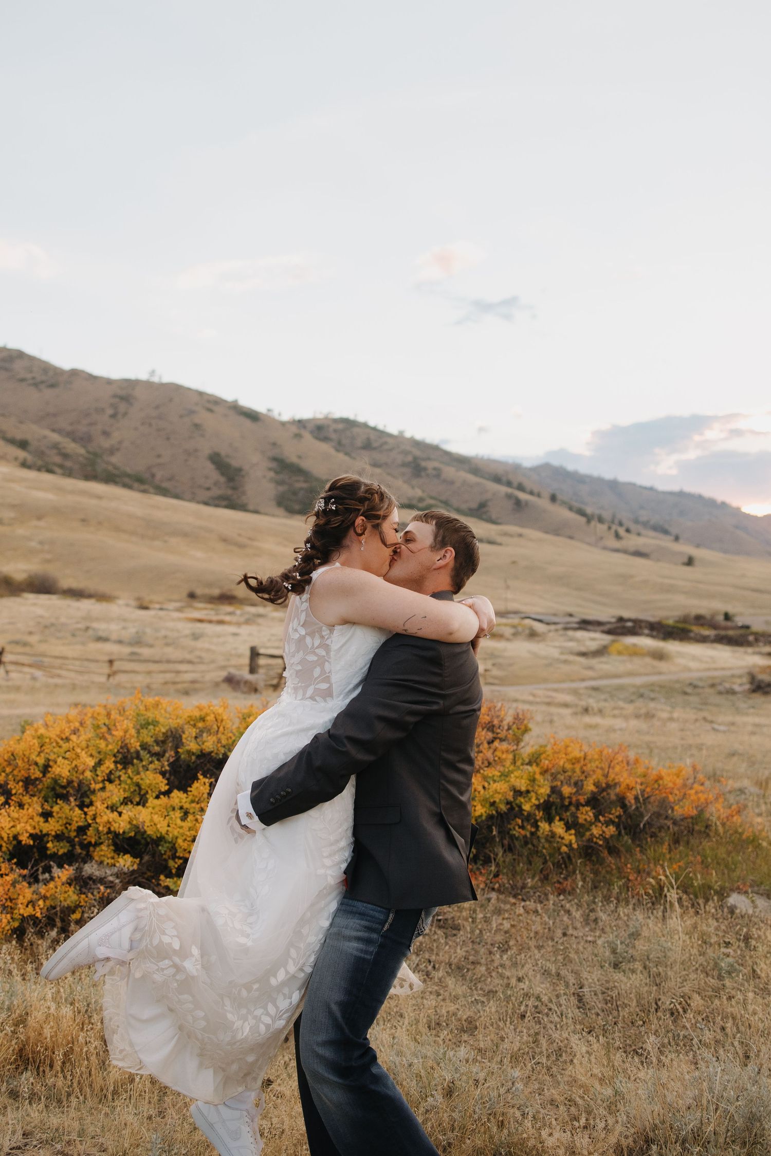 Groom lifts bride for a kiss in open field with colorful autumn mountain scenery. Wyoming wedding.