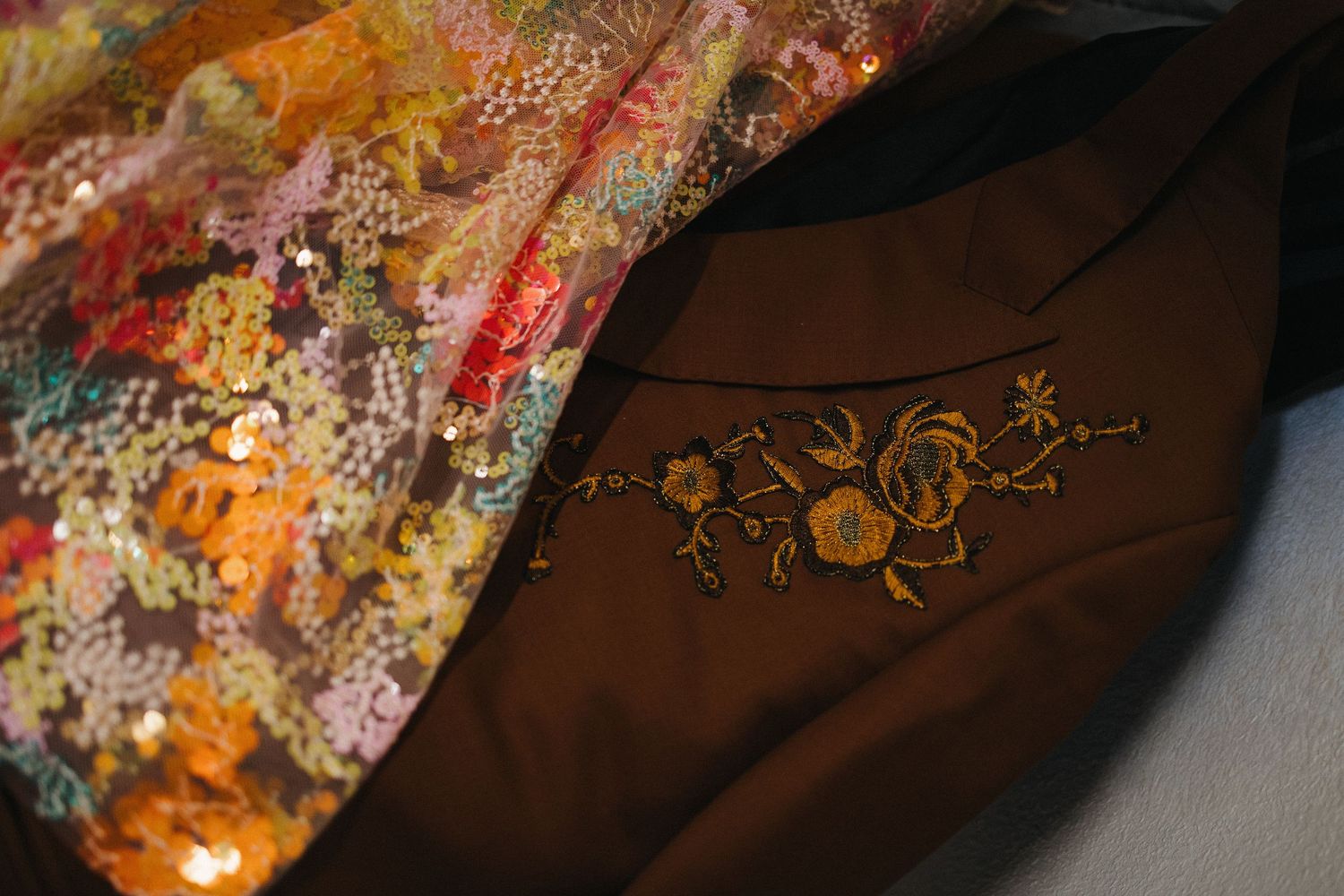 Close-up of brown fabric with gold floral embroidery beside colorful sequined textile detail.