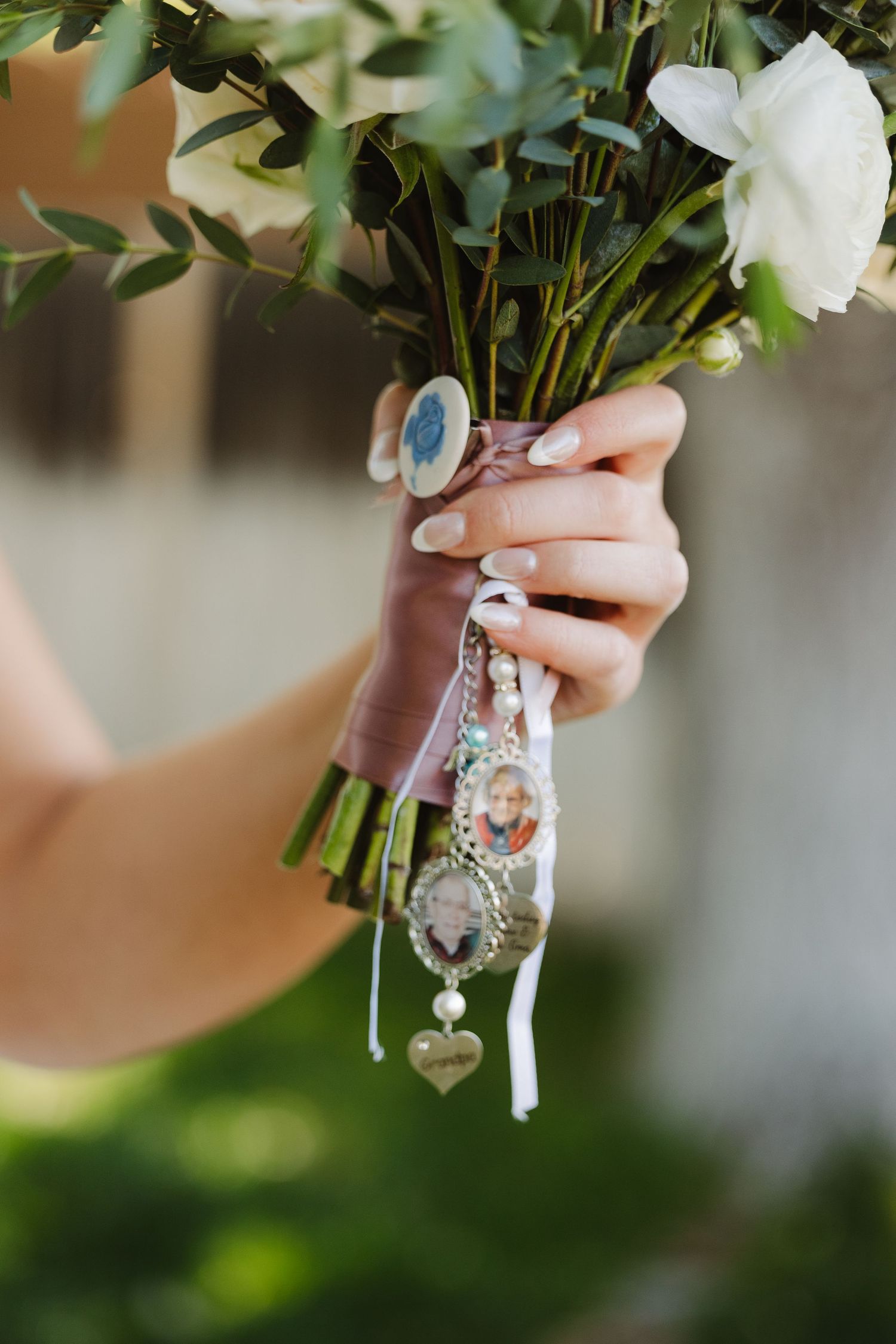 Bride holds white floral bouquet adorned with memorial photo charms and ribbon keepsakes.