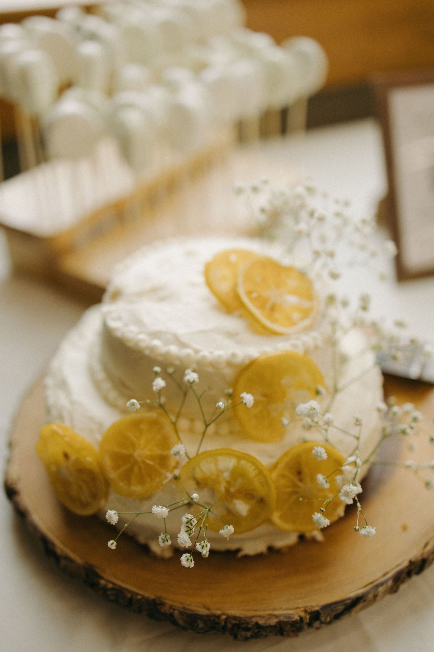 Elegant two-tier white wedding cake decorated with dried lemon slices and baby's breath on wood slab.