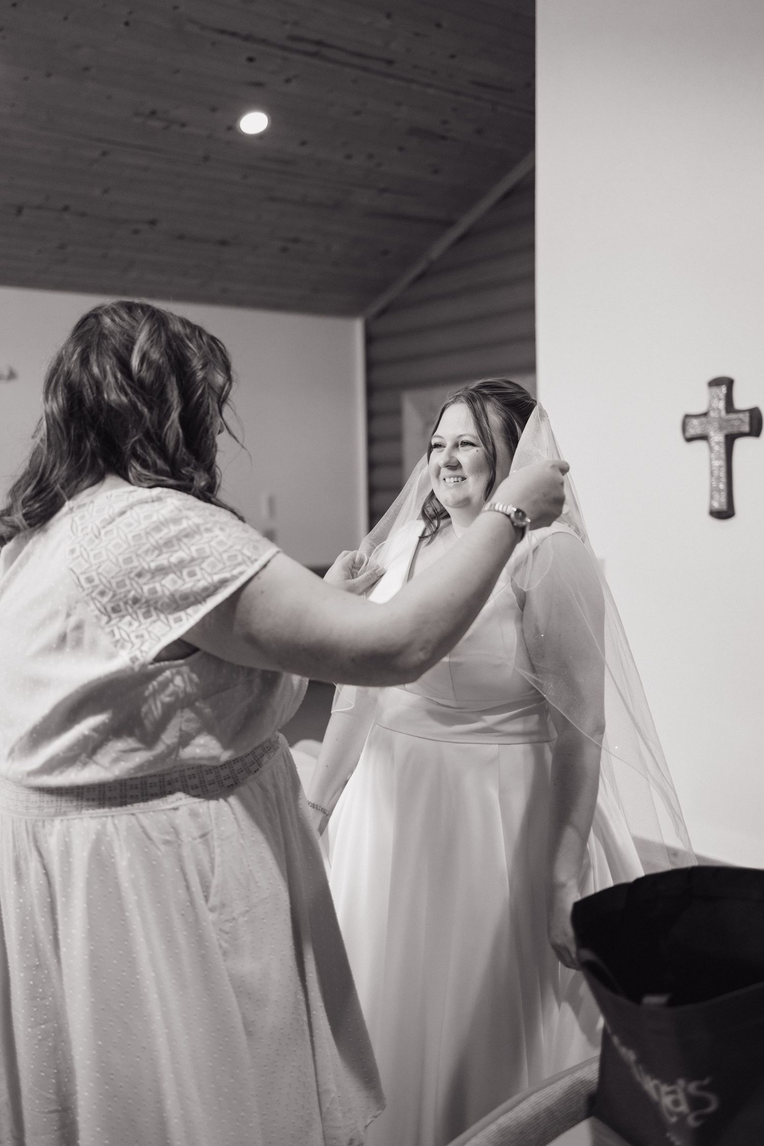 Bridesmaid adjusts brides veil in black and white photo inside a rustic log cabin wedding chapel.