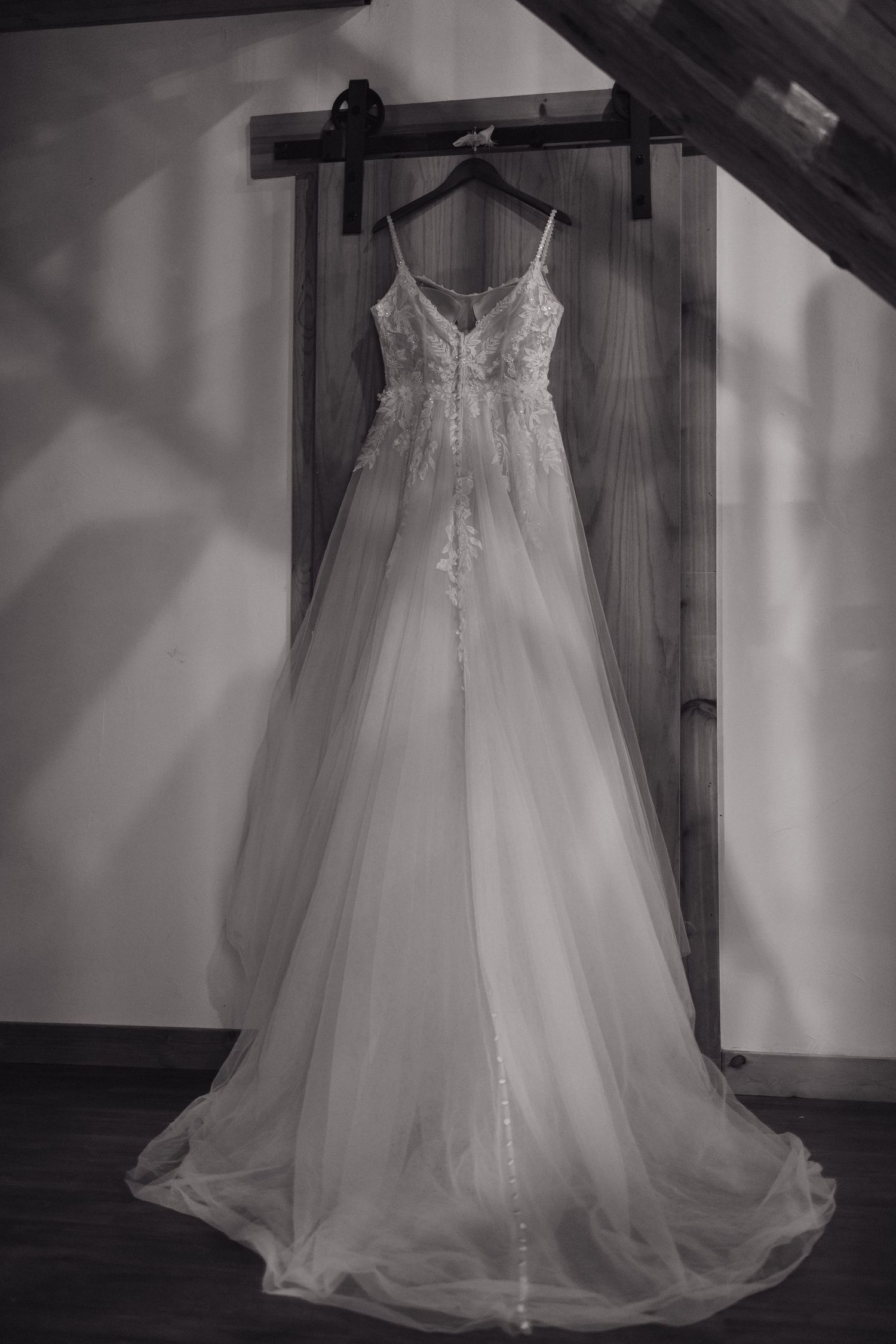 Elegant lace A-line wedding gown hanging on a barn door in black and white photo.