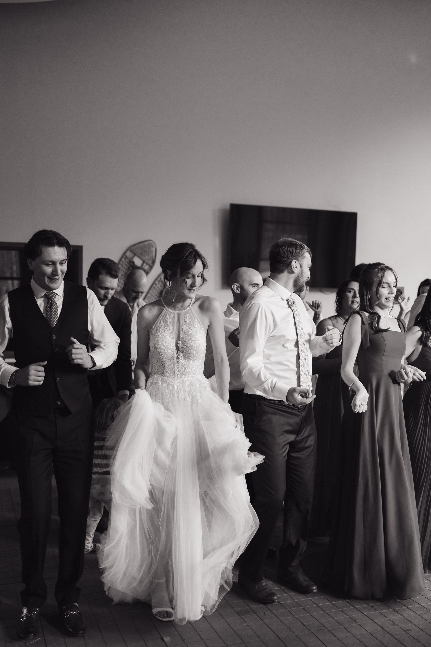 Black and white photo of bride in halter gown dancing with wedding party guests at reception.