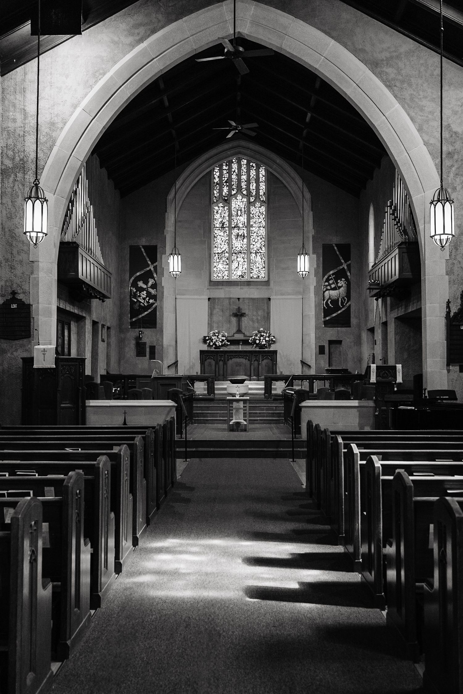 Black and white interior of an empty church with wooden pews and stained glass.