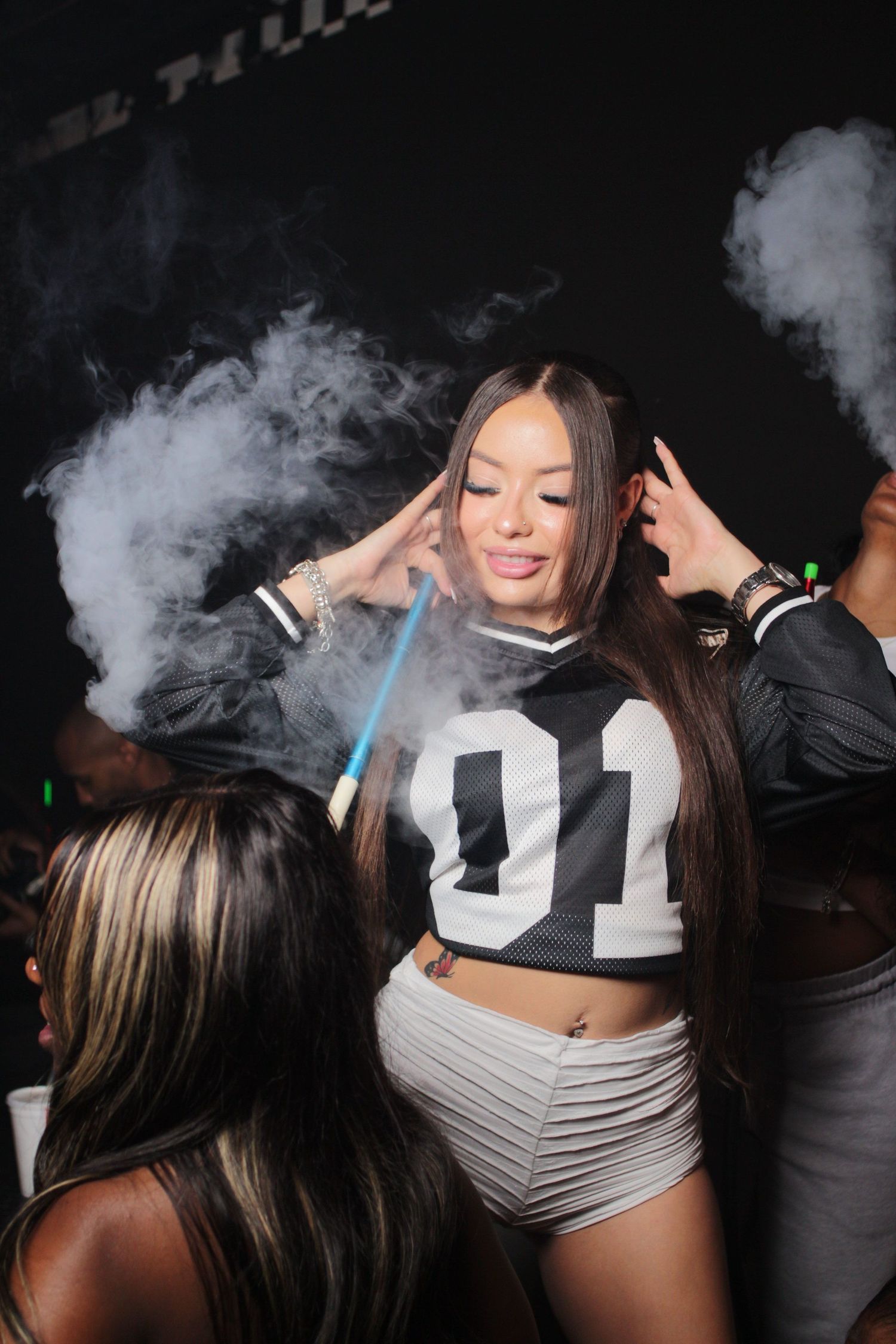Person dancing in a crop top and shorts surrounded by smoke effects at a club.