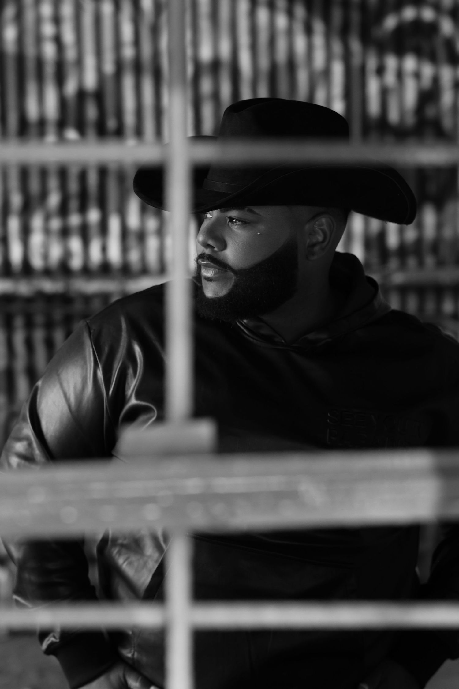Black and white portrait of a bearded man in a cowboy hat and leather jacket, looking away thoughtfully.