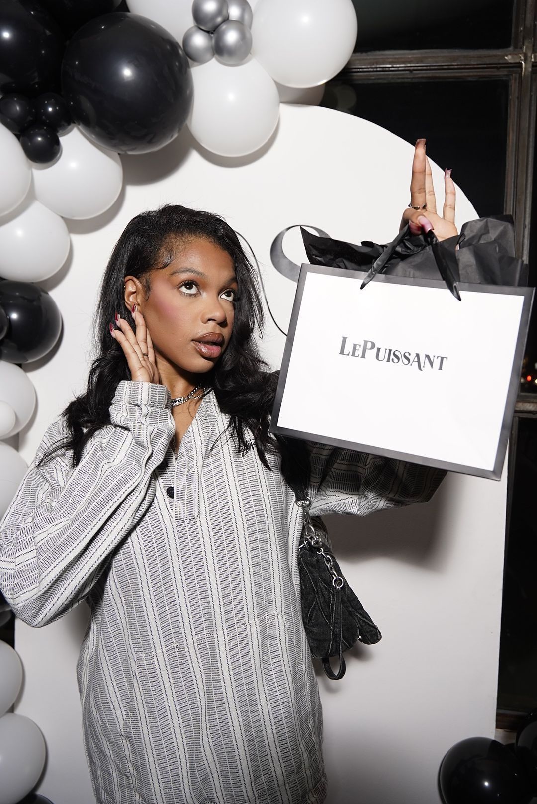 Model poses with black and white balloons wearing a striped top and holding shopping bags in a stylish photoshoot series.