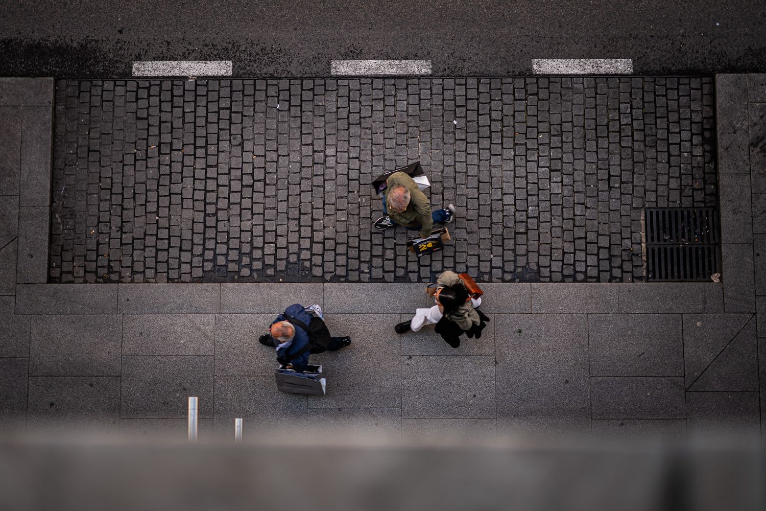 Aerial view of three pedestrians walking on cobblestone and concrete city sidewalk.