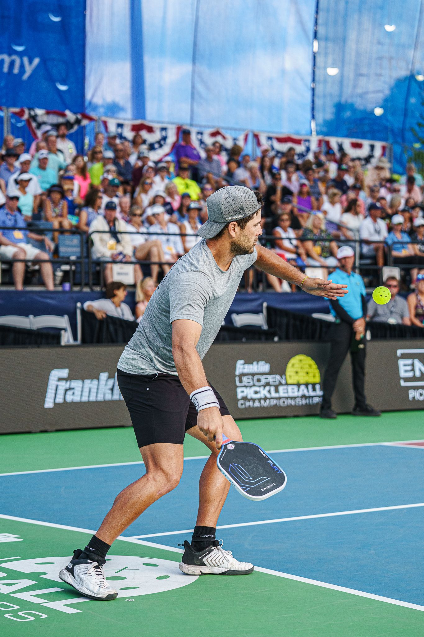 Male pickleball player in gray shirt returns a shot before a packed crowd at the US Open.