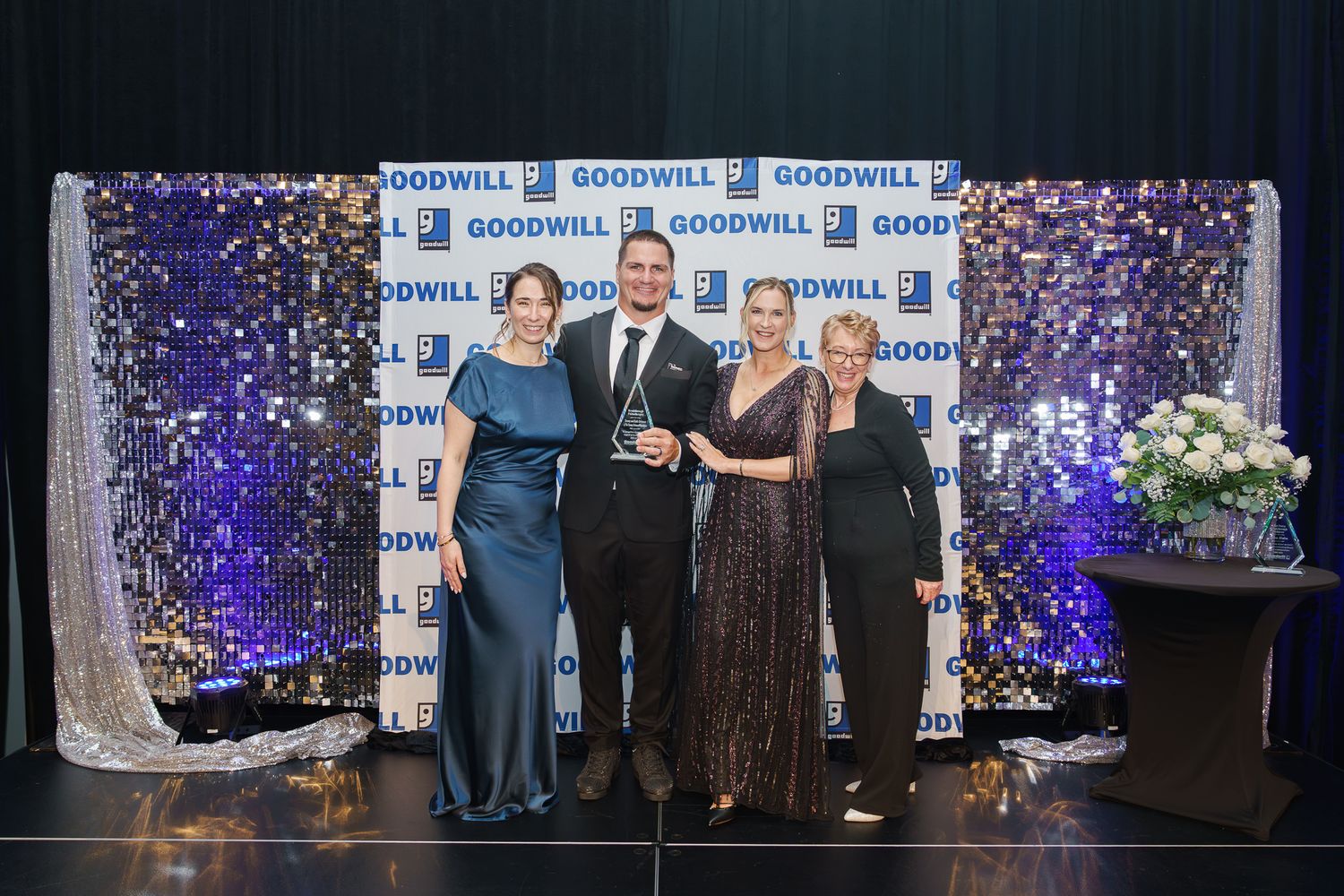 Four people pose together in formal attire in front of a Goodwill step-and-repeat banner.