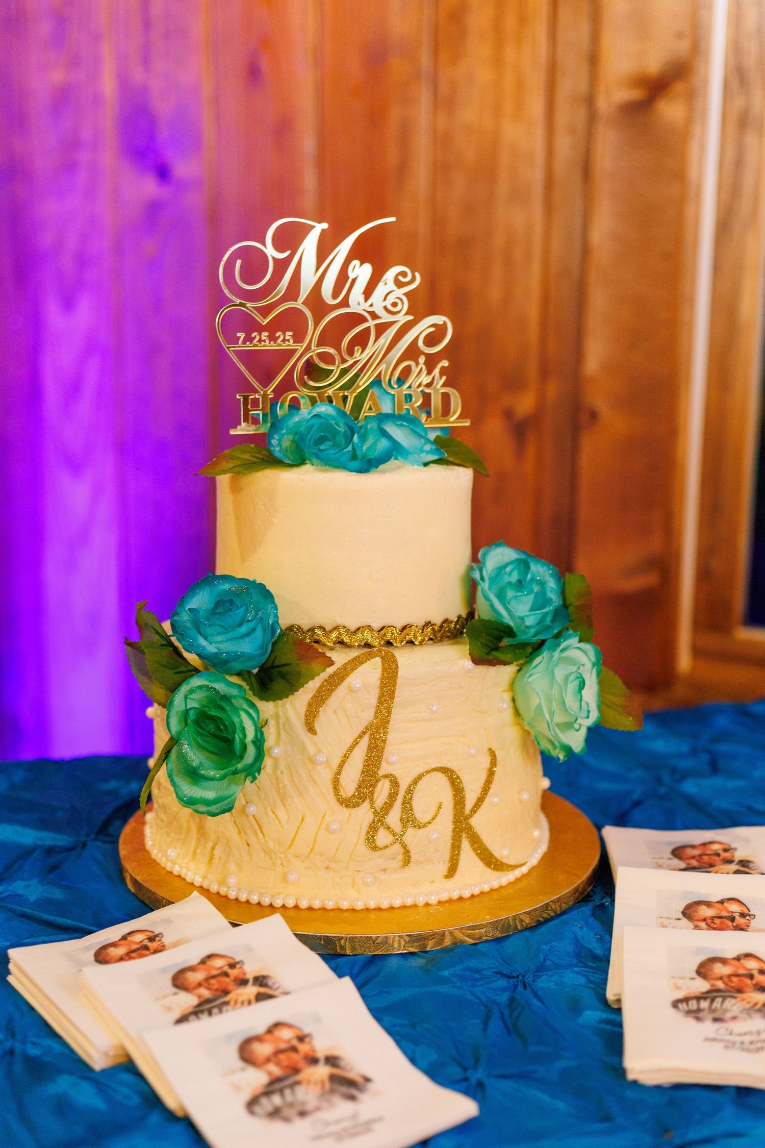Two-tier white wedding cake with teal roses and Mr. and Mrs. Howard gold cake topper.