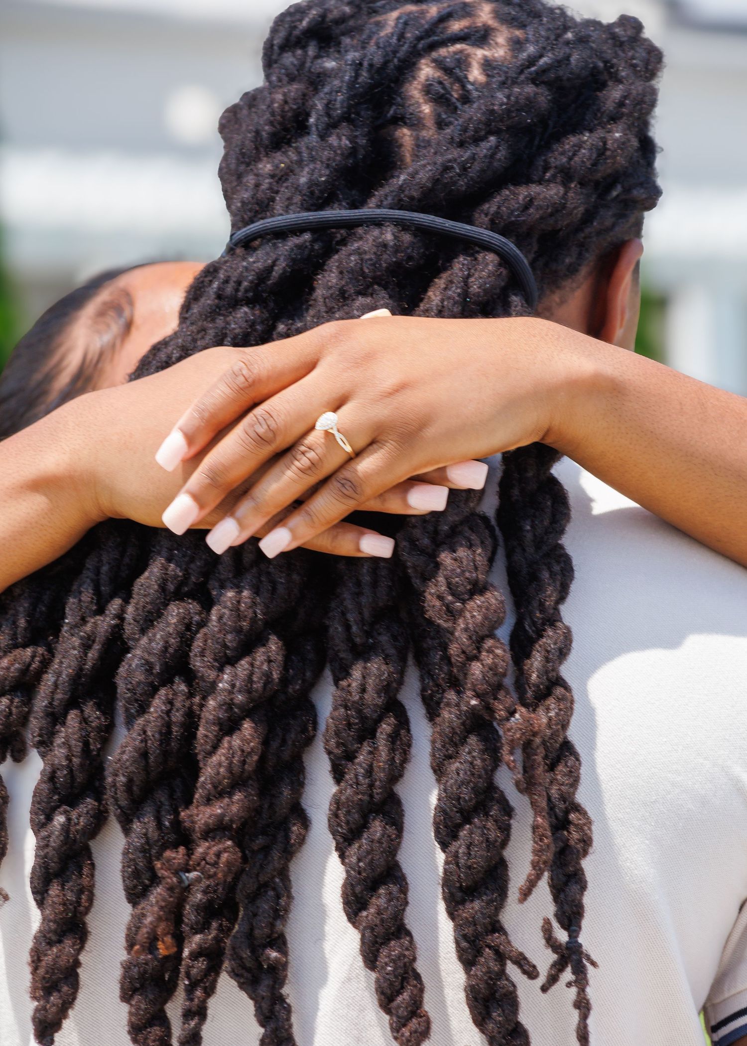 Close-up of a womans hand with engagement ring resting on mans twisted locs hairstyle.