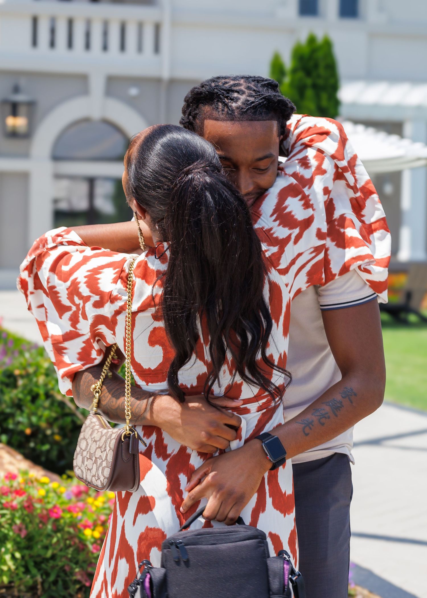 Joyful couple hugging tightly outdoors near colorful flowers after an emotional proposal moment.