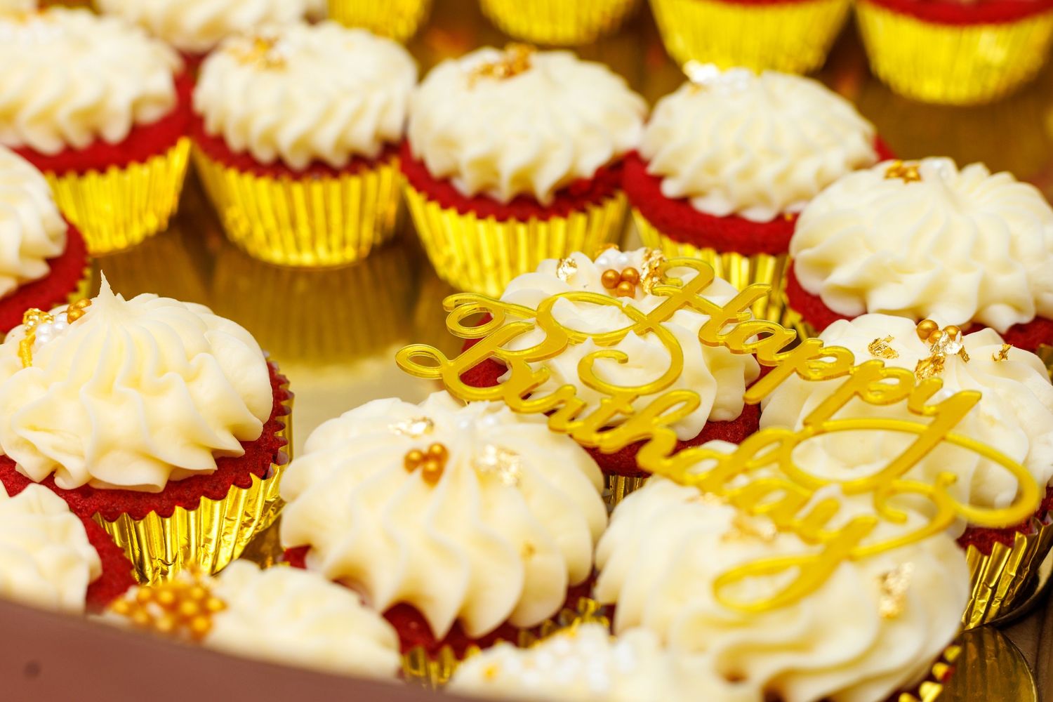 Red velvet cupcakes with white frosting in gold wrappers with a Happy Birthday topper.