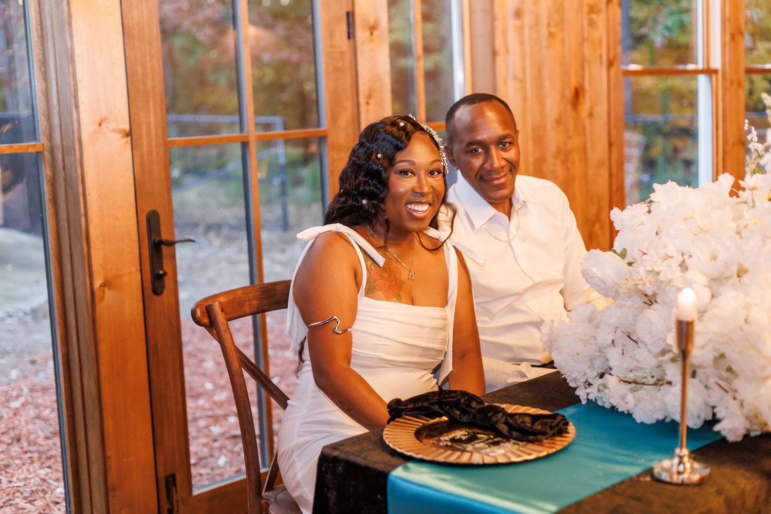 Happy couple smiling together at their wedding reception table with white floral arrangements.