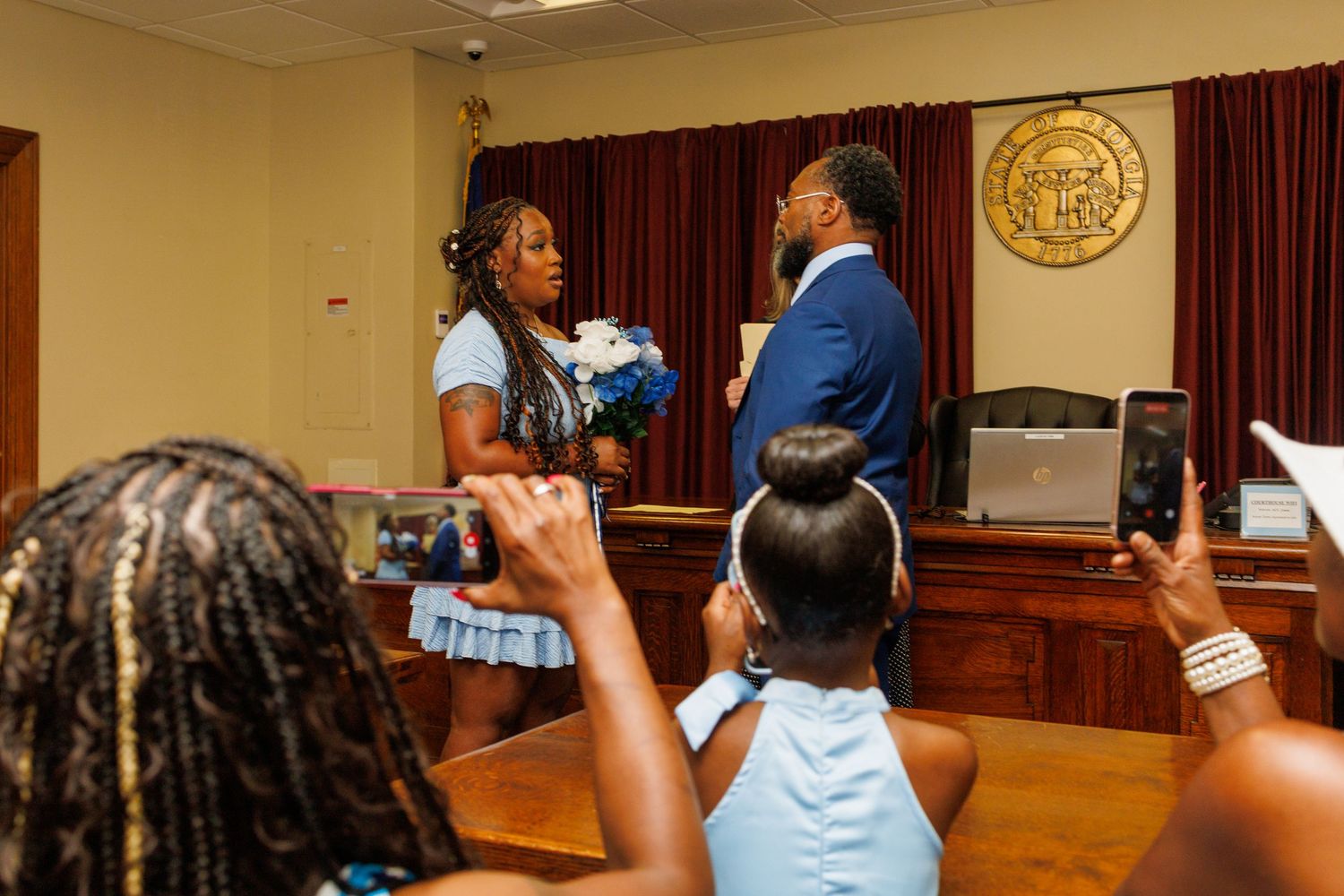 Couple exchanging vows at a courthouse wedding ceremony with guests watching and recording.